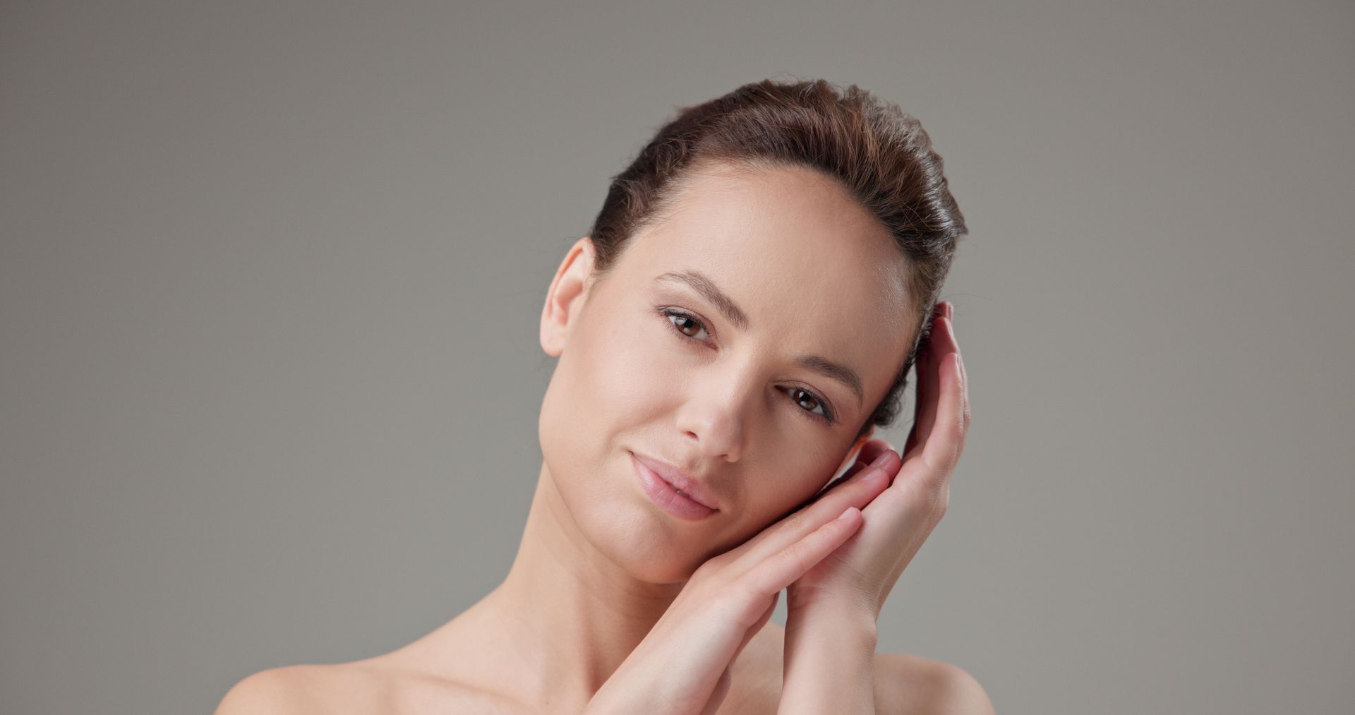 A woman is touching her face with her hands and smiling.