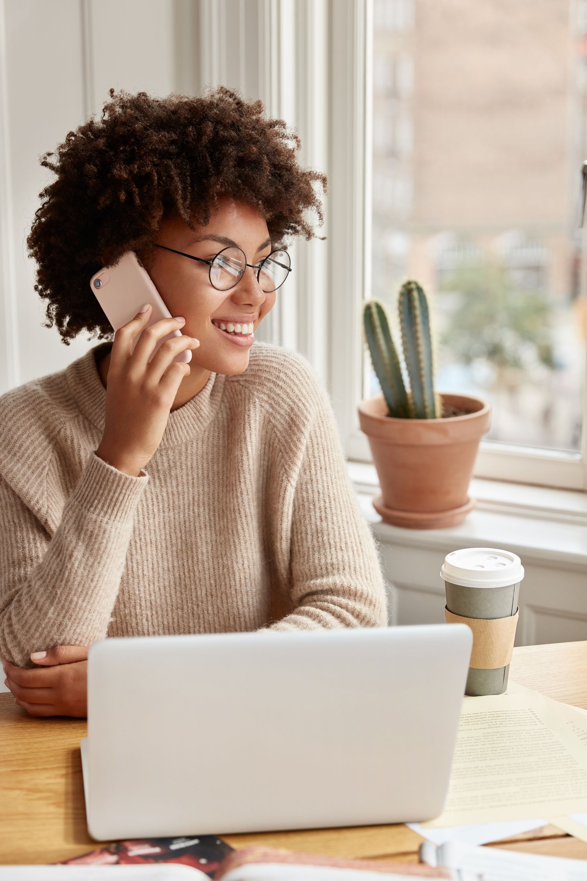 A woman is sitting at a desk with a laptop and talking on a cell phone.