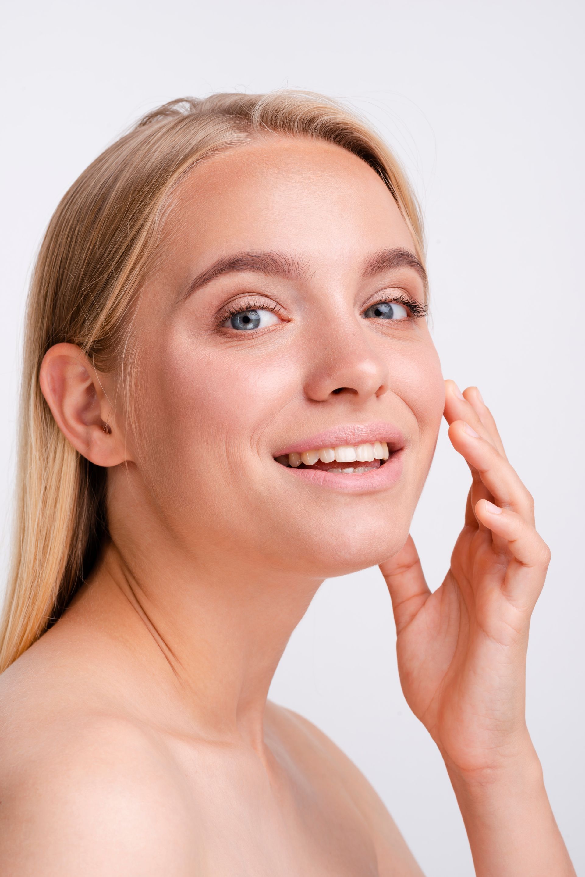 A woman is touching her face with her hand and smiling.