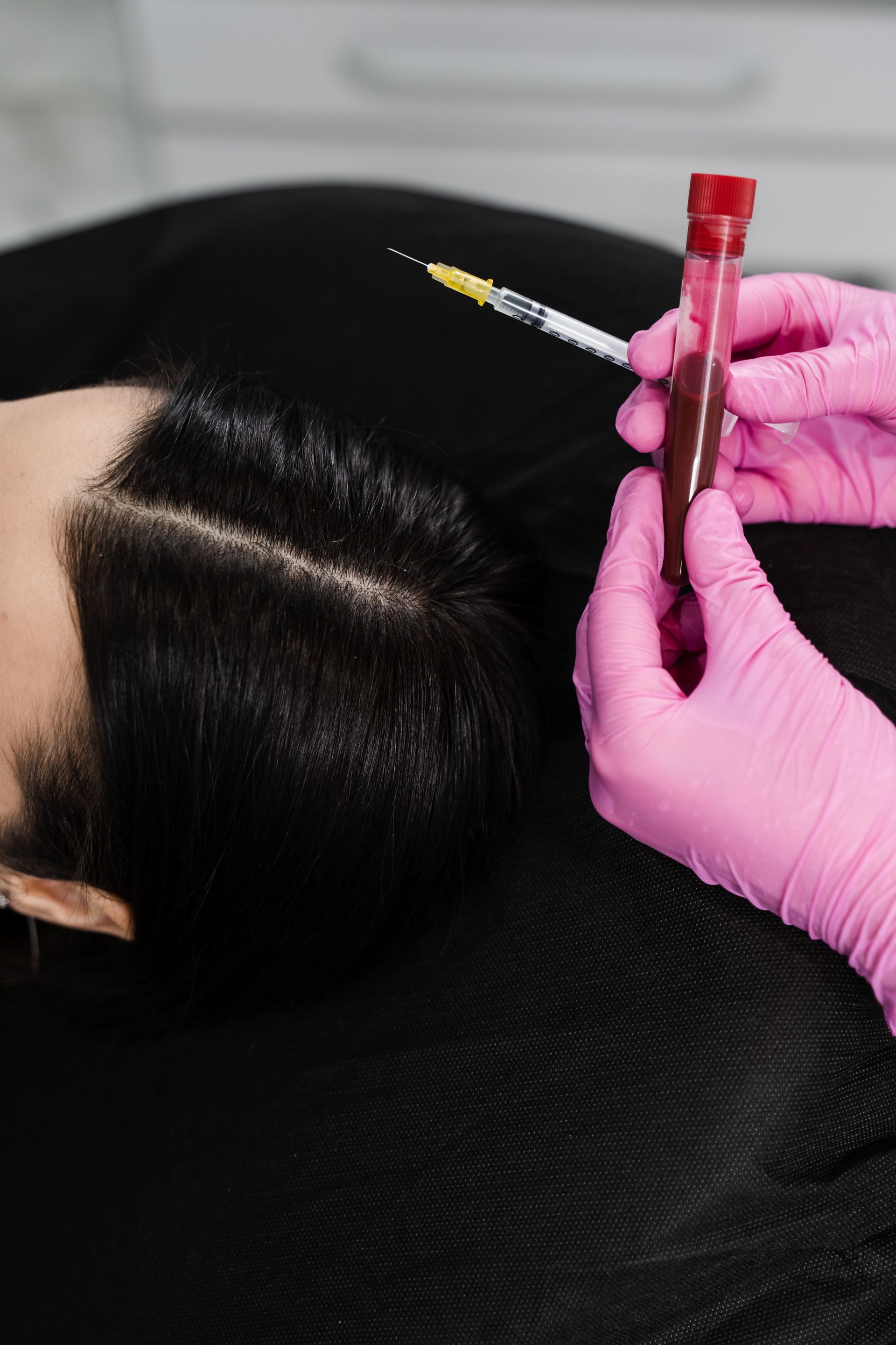 A woman is getting an injection in her hair while wearing pink gloves.