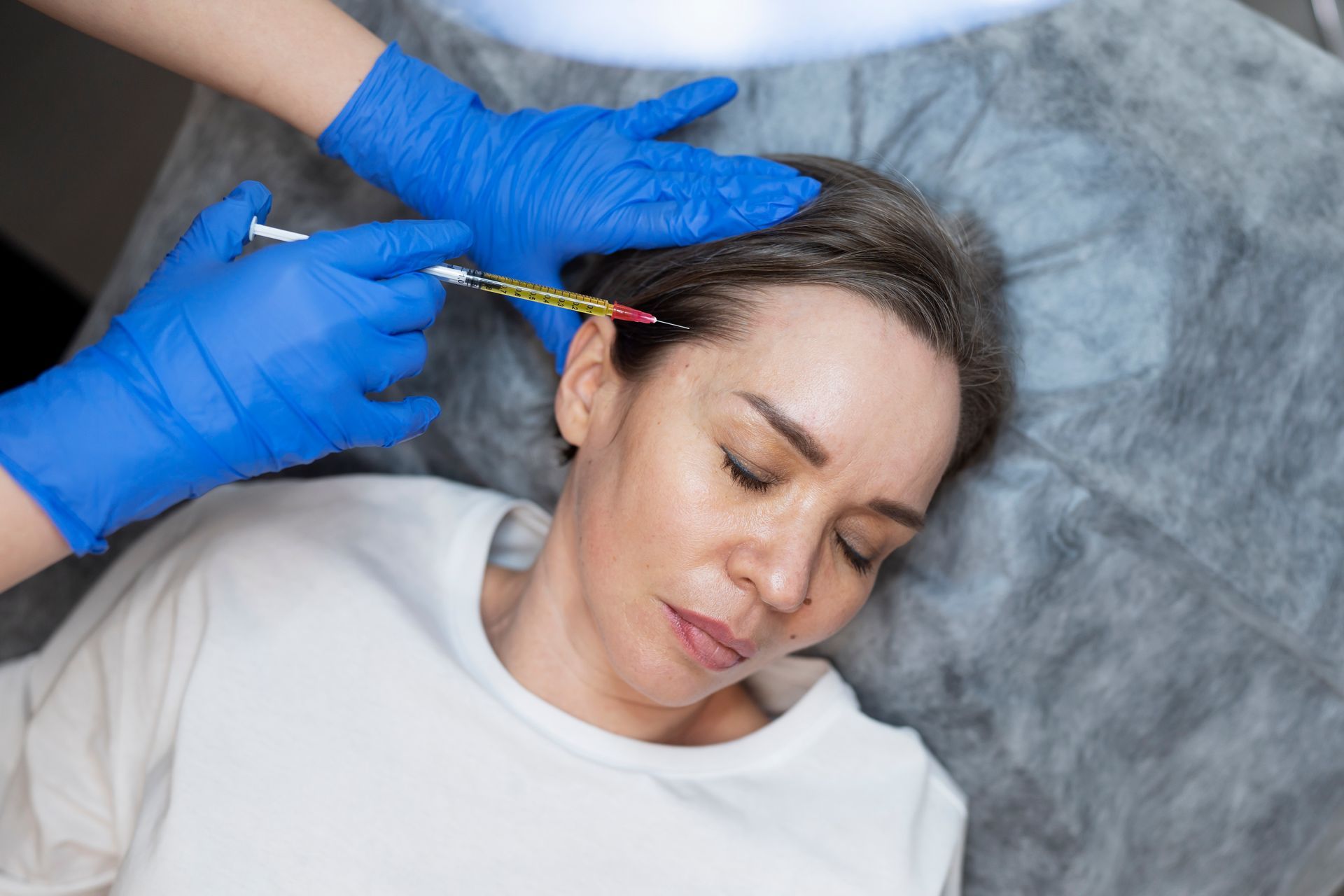 A woman is getting a botox injection in her head.