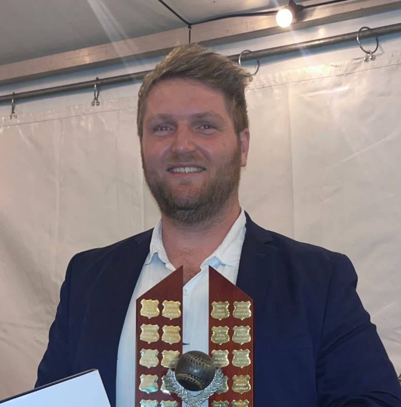 Man in a blue suit holding a red award plaque, smiling under a white event tent.— Moreton Bay Therapy in Deception Bay, QLD
