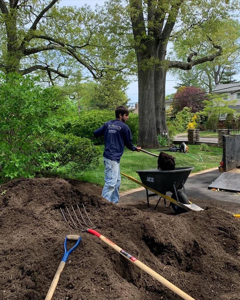A man is standing in a pile of dirt next to a wheelbarrow.