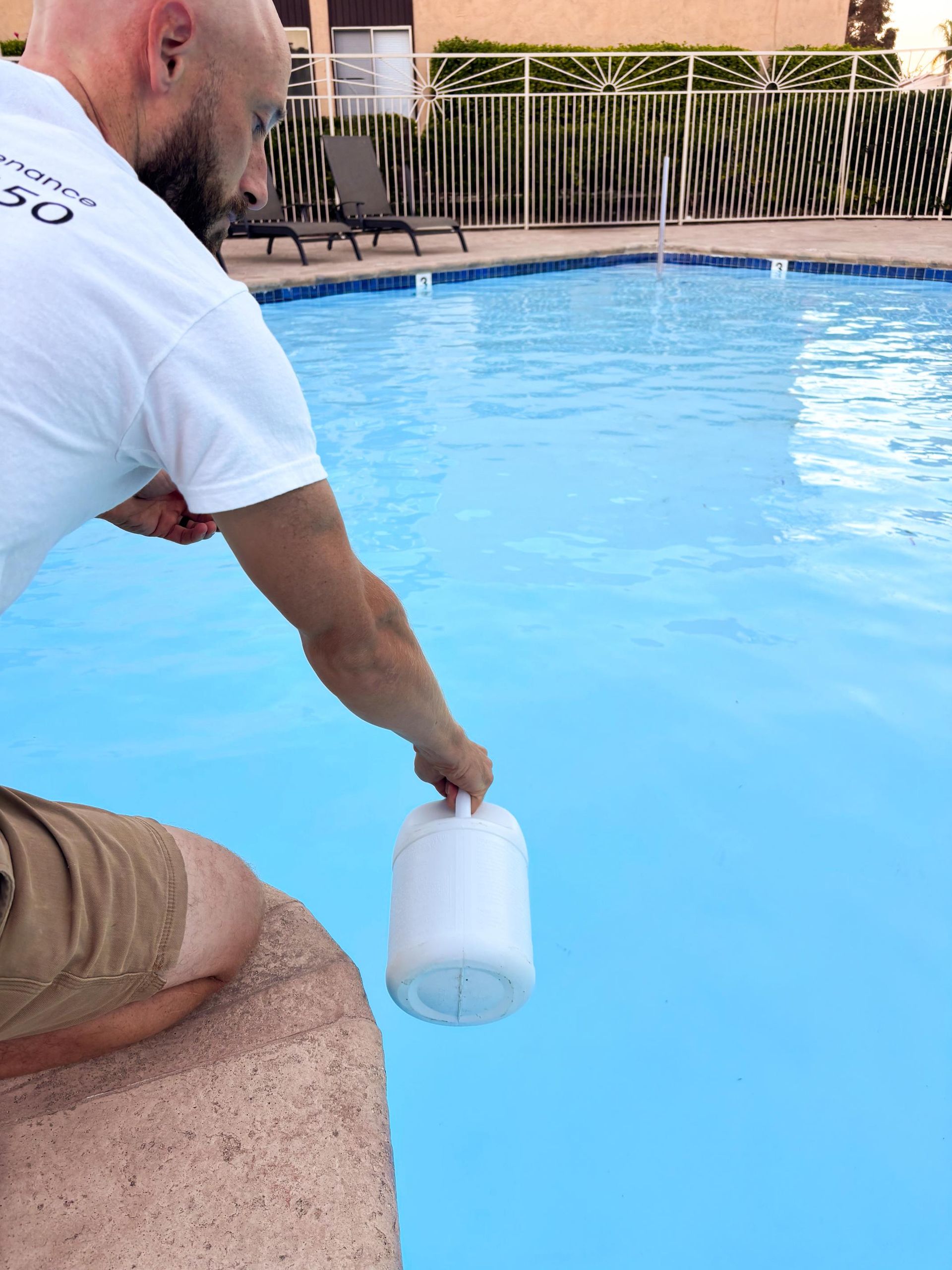 A man in a white shirt is kneeling next to a swimming pool
