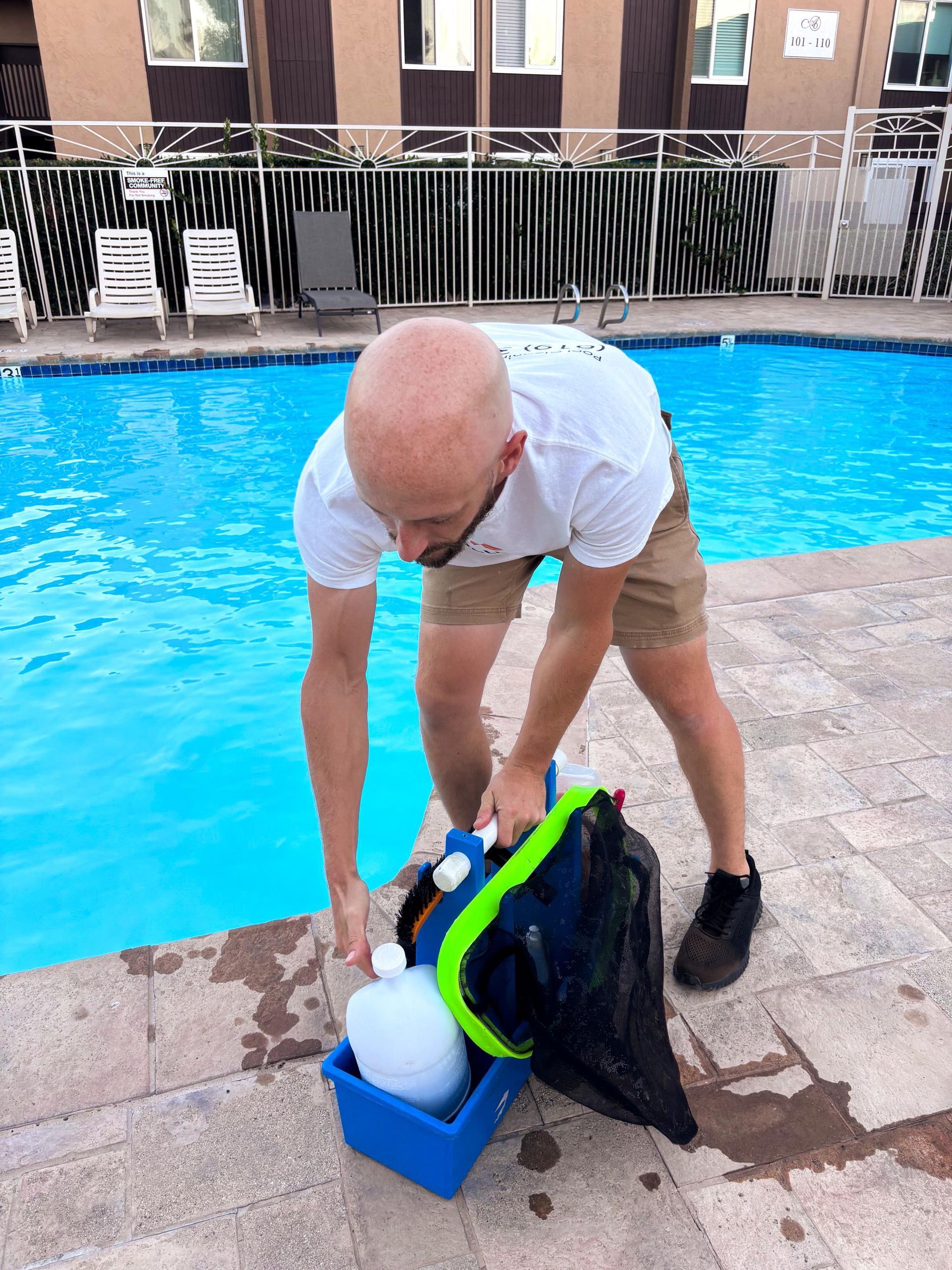 A bald man is standing next to a swimming pool.