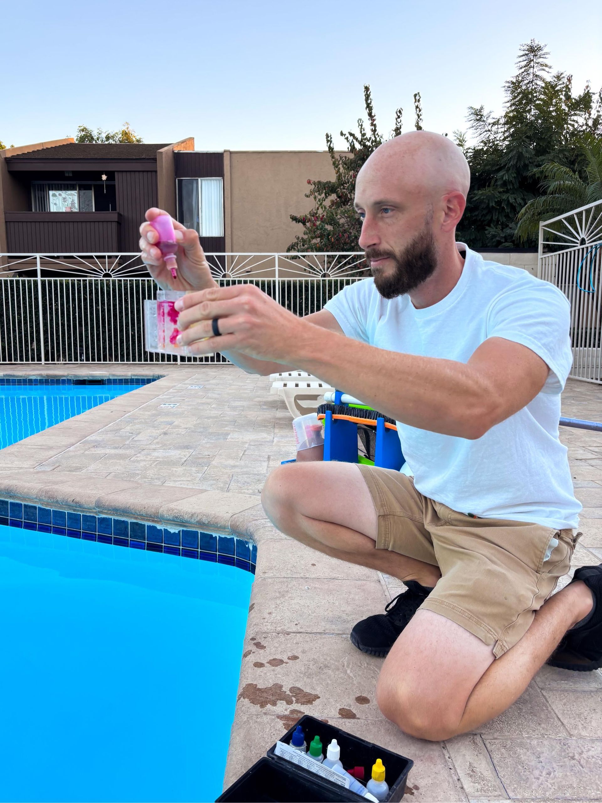 A man is kneeling on the edge of a swimming pool.