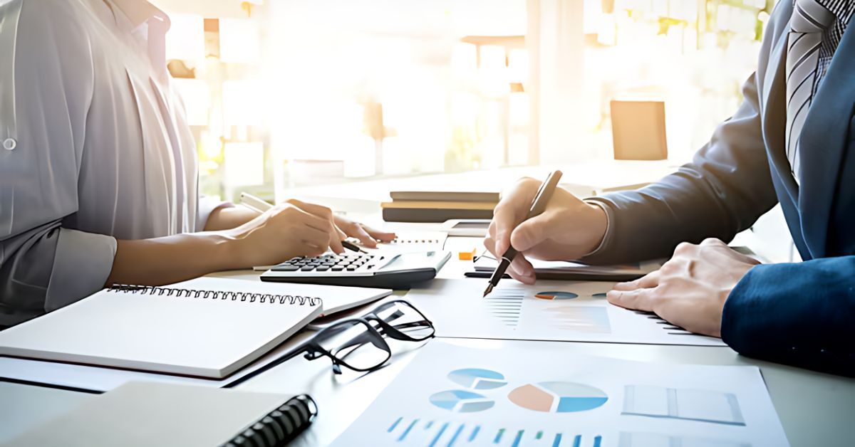 A man and a woman in business attire, going over financial documents at a desk.