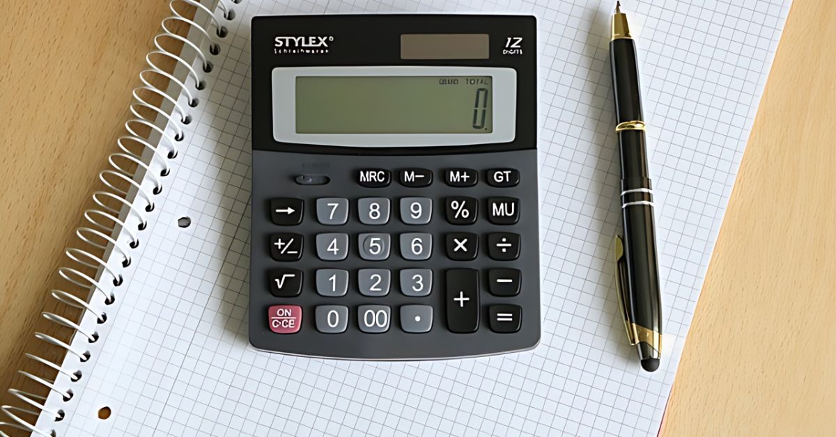 A calculator and pen sitting on a notebook with graph paper.