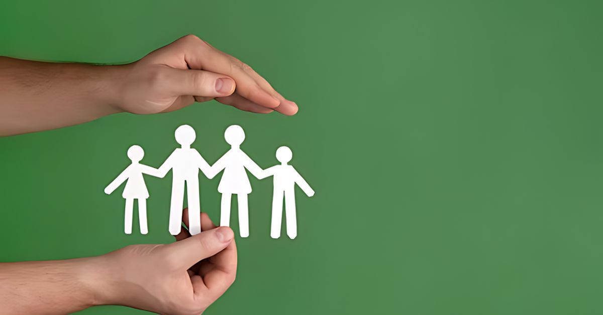 Hands protecting a cutout paper family on a green background.