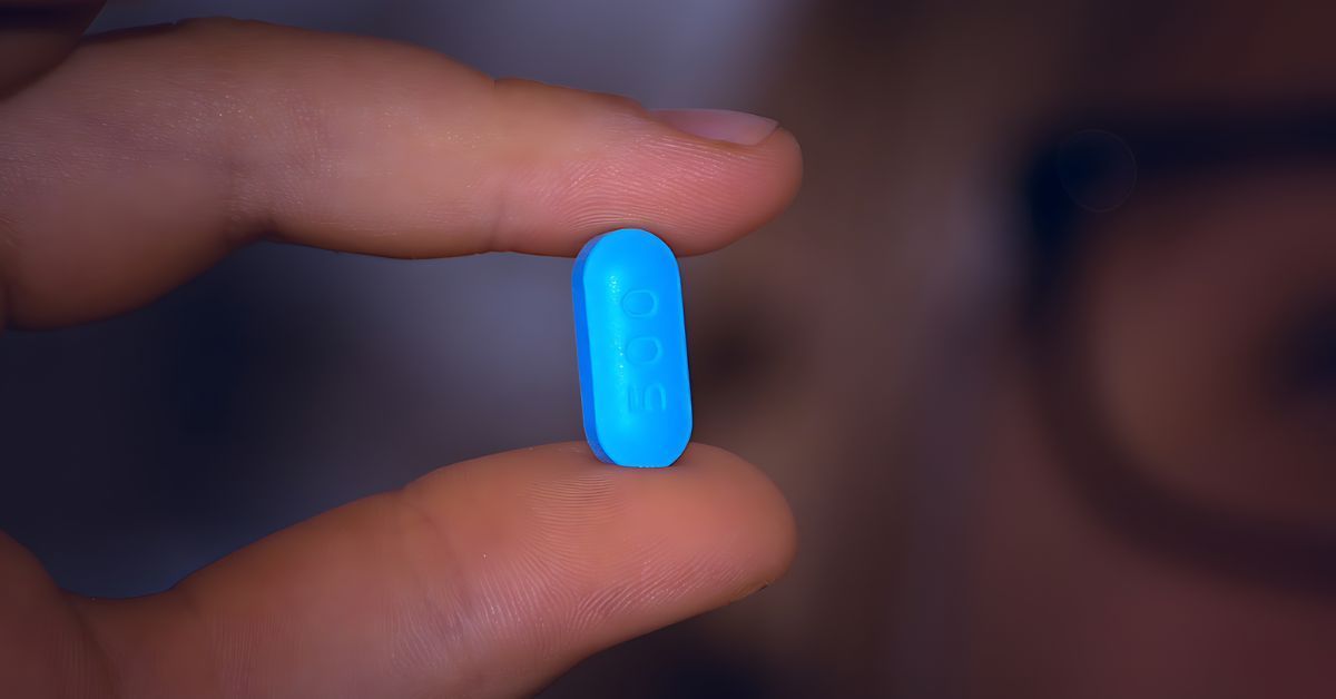 A person holding a small, blue pill.