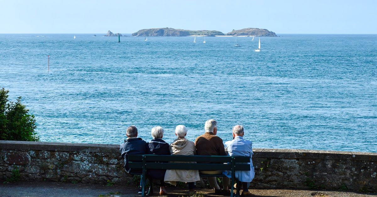 Retired Senior friends are sitting next to the ocean.