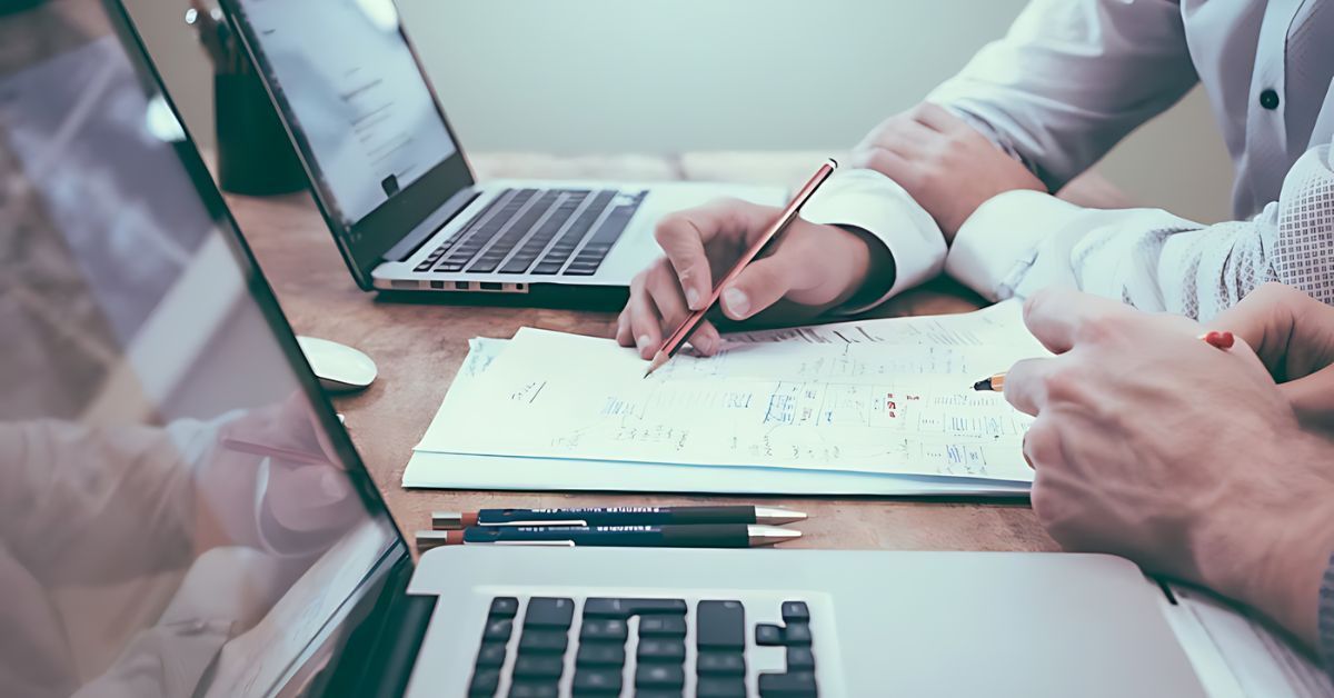 Retirement planner working out a plan on pen and paper with laptops nearby.