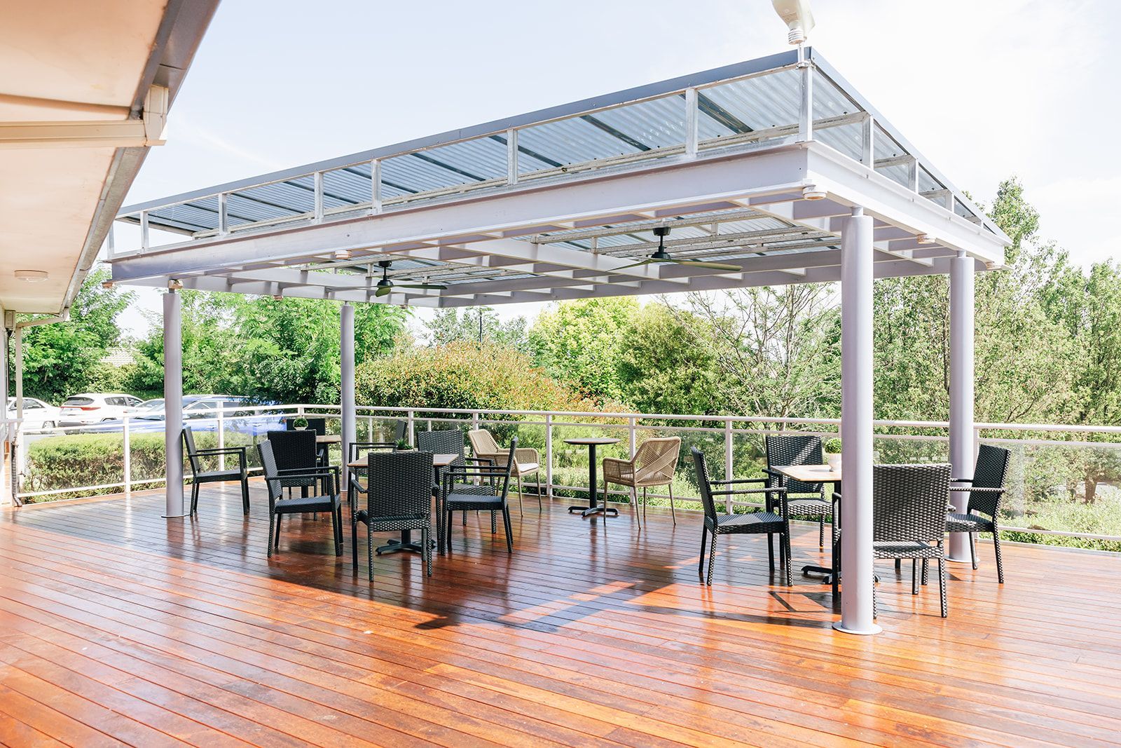 A wooden deck with a covered outdoor patio area featuring black chairs, small tables, and a view of greenery.