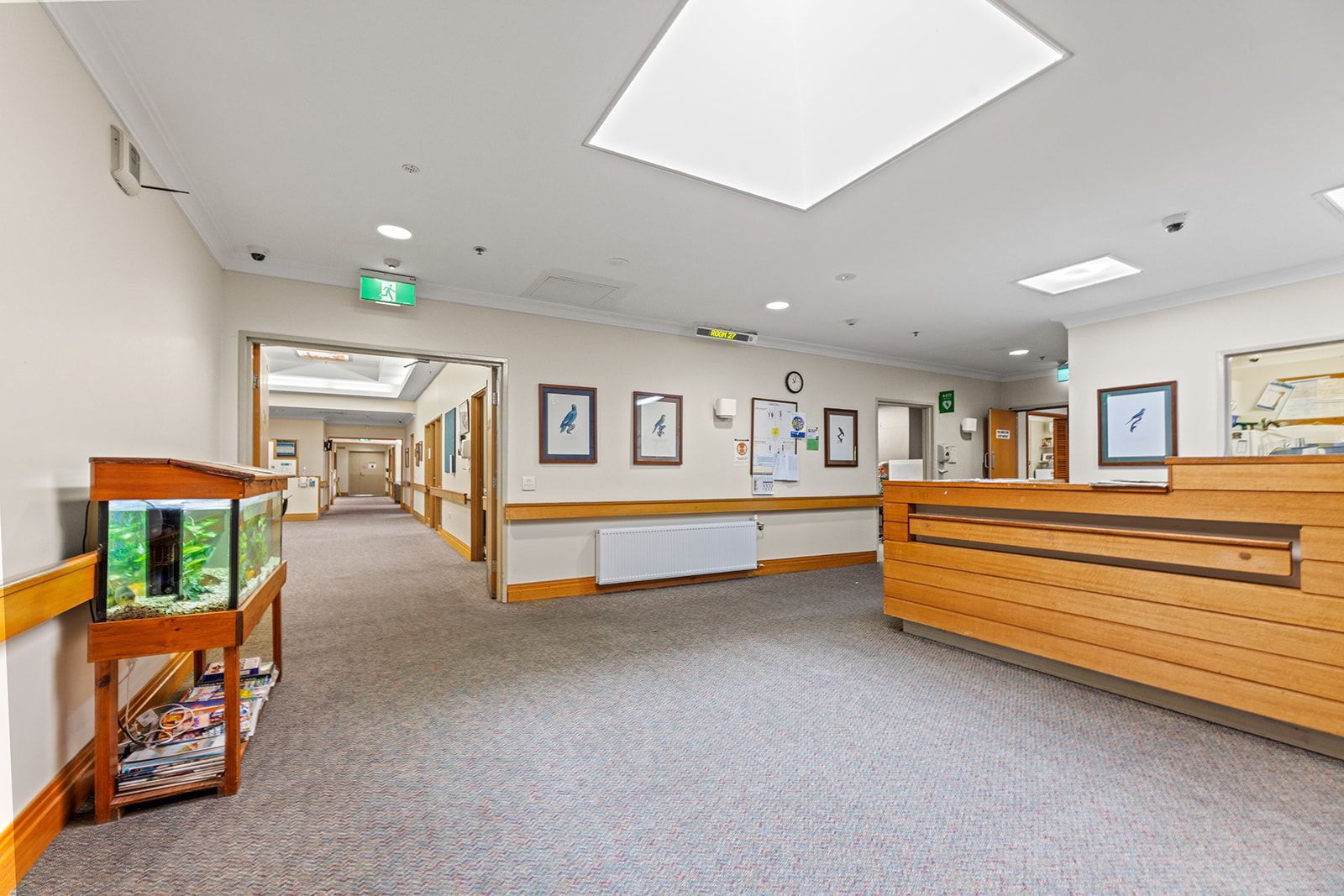 An interior view of a facility hallway with a wooden reception desk, a fish tank on a stand, and framed wall art.