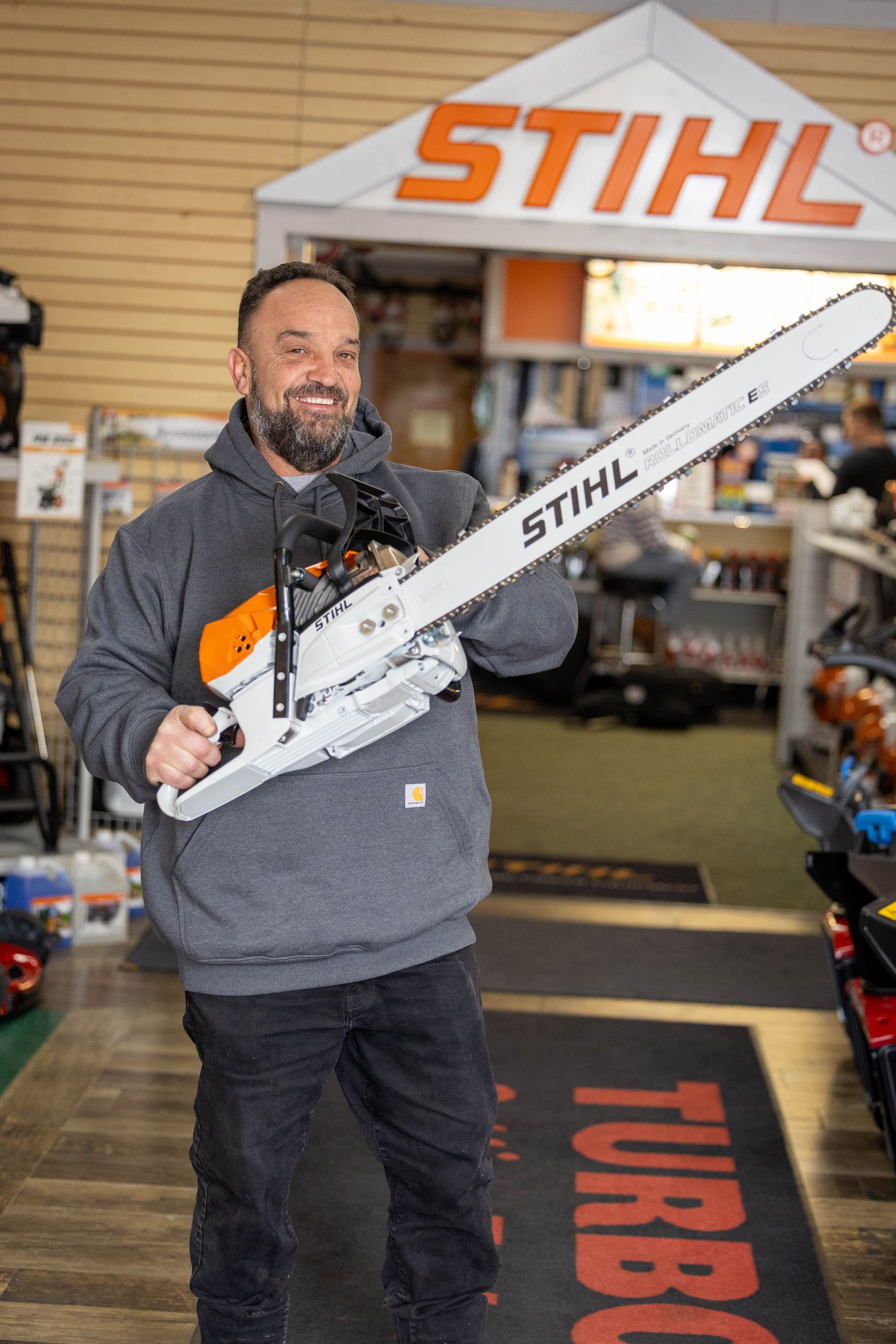A man smiling and holding up a chainsaw