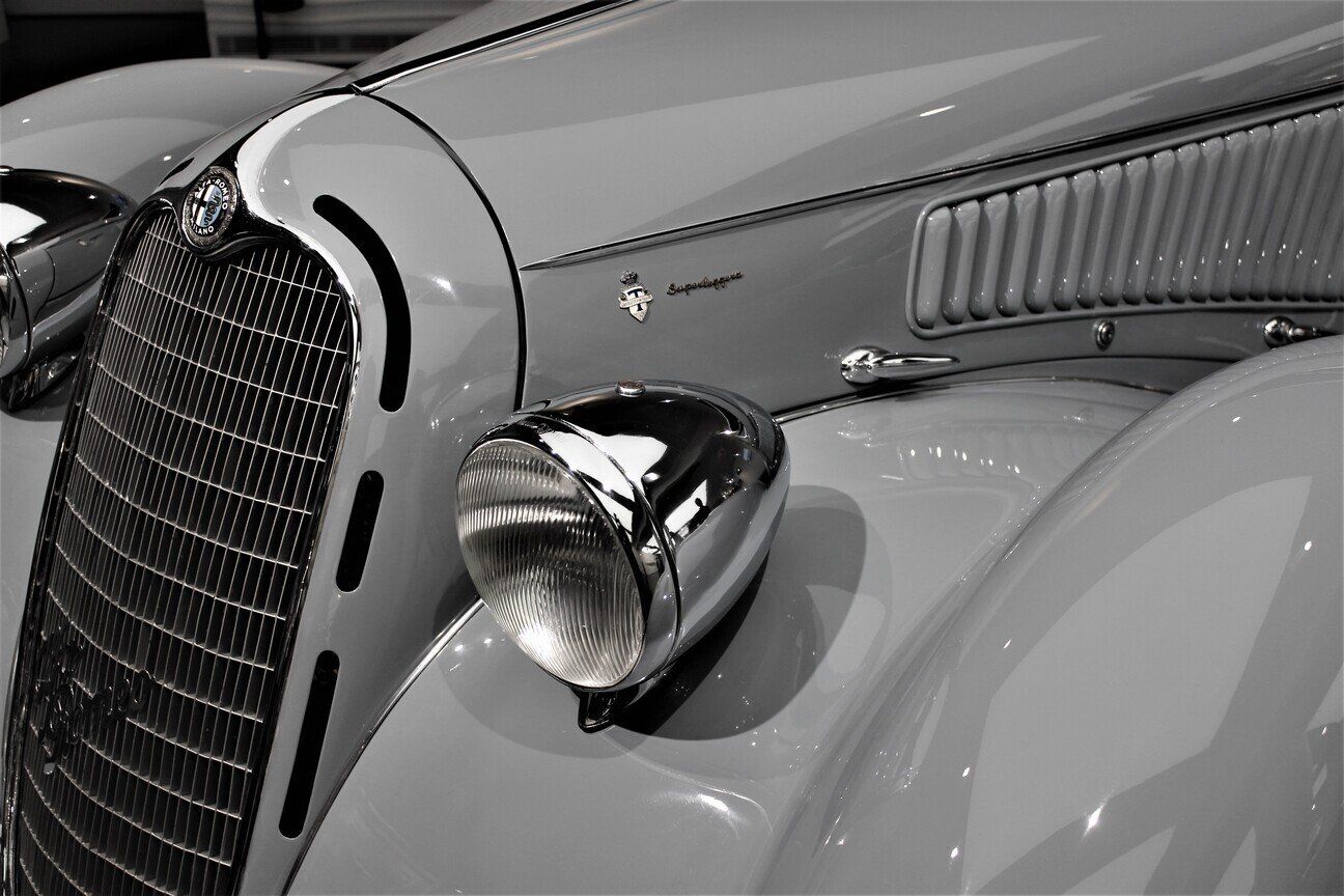 Two freshly polished roadster motorcycles parked beside the beach at sunset, a 100-spoke chrome wheel, detailing technician polishing front fender of blue sedan, freshly detailed greyscale image of studebaker