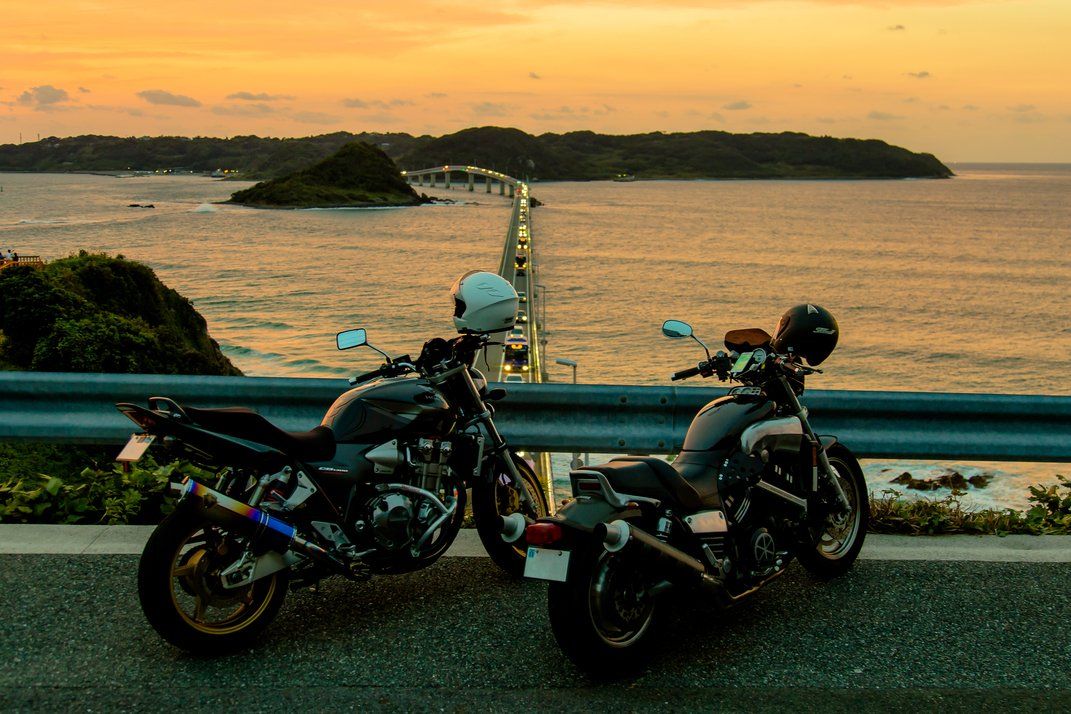 Two freshly polished roadster motorcycles parked beside the beach at sunset