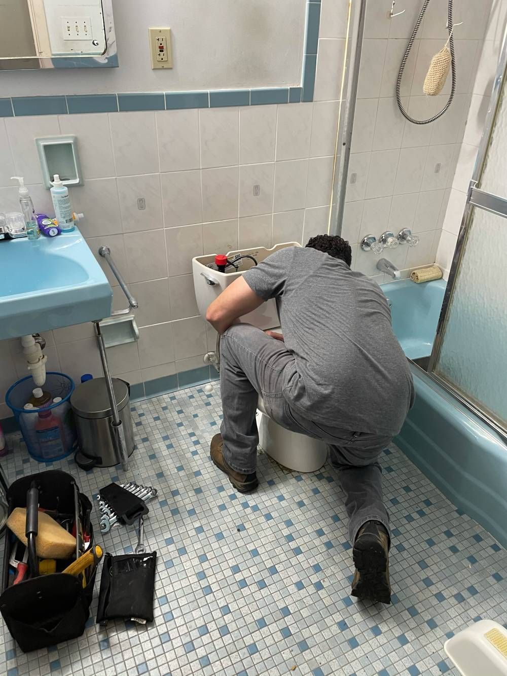 A man is kneeling on a toilet in a bathroom.
