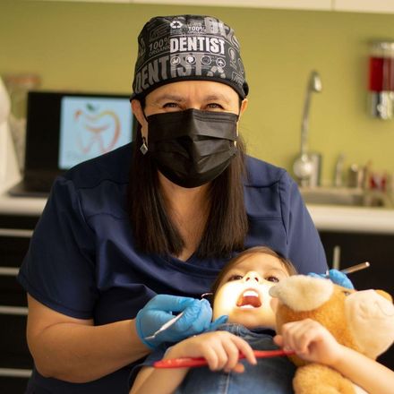 Una mujer que lleva un gorro de dentista está cepillando los dientes de un niño.
