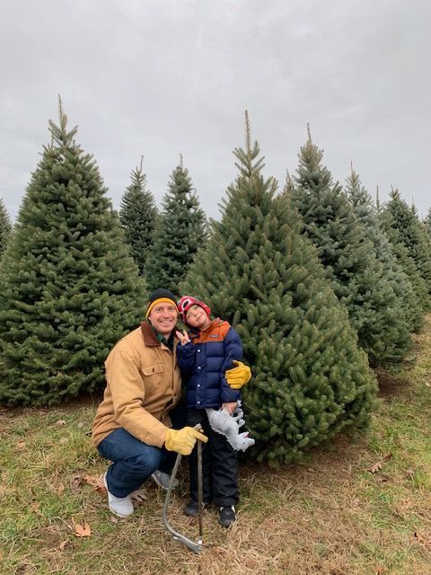 A man and a child are kneeling in a field of christmas trees.