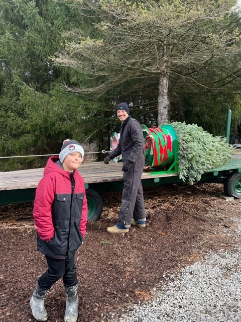 Two people are standing next to a trailer with a christmas tree on it.