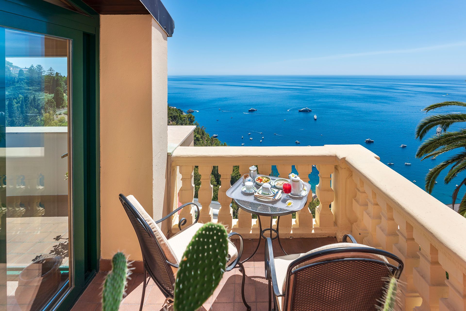 Balcony table with drinks overlooking a bright blue ocean and coastal view