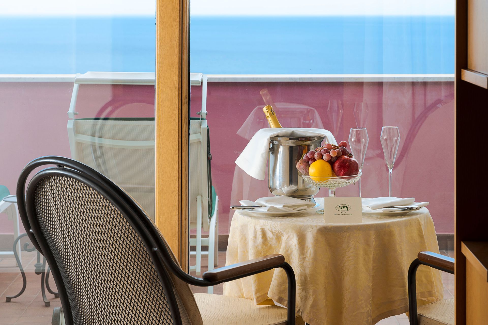 Balcony dining table with fruit and drinks overlooking the ocean, with chairs in the foreground