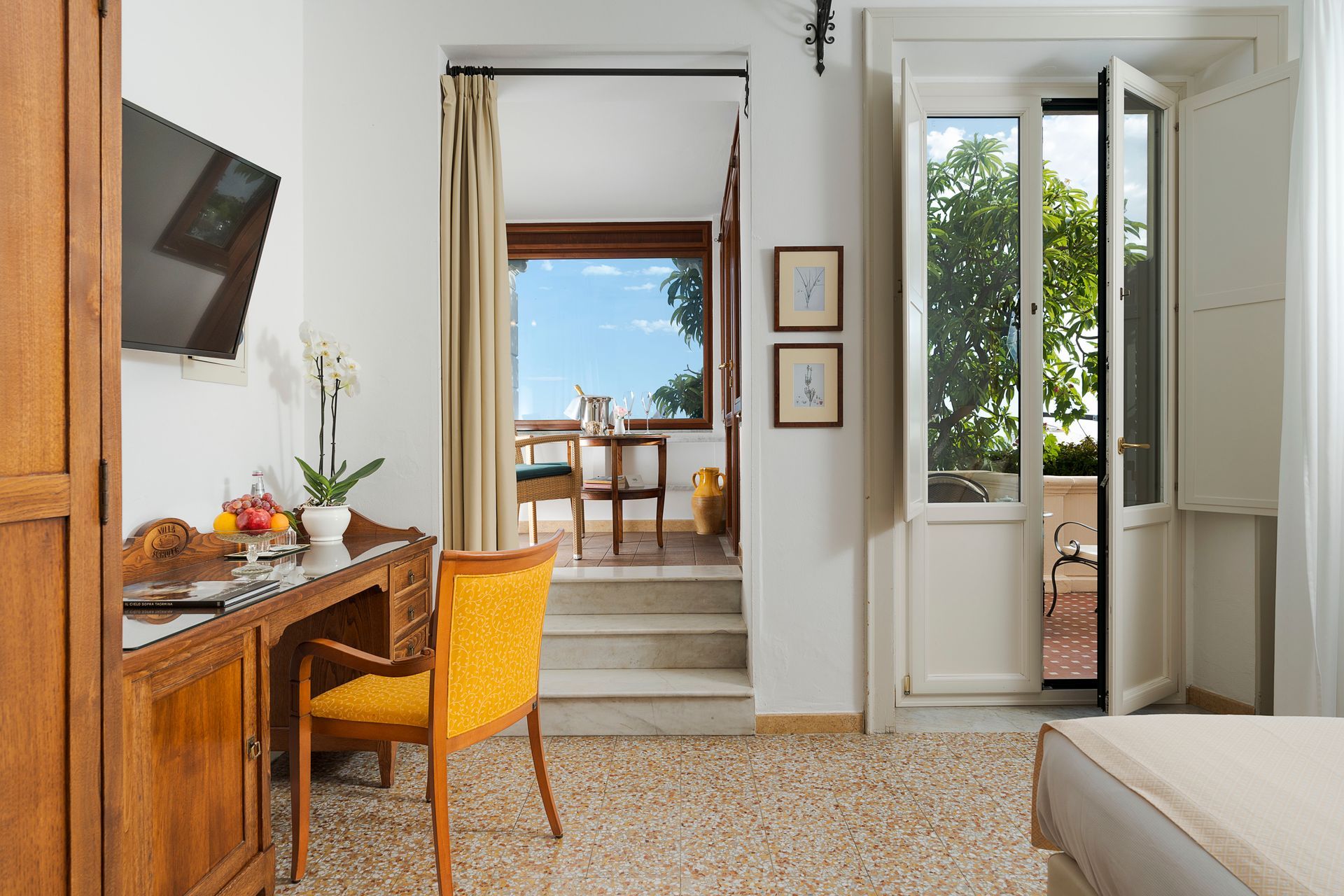 Bright bedroom with desk, yellow chair, open doors to balcony, and sea view outside