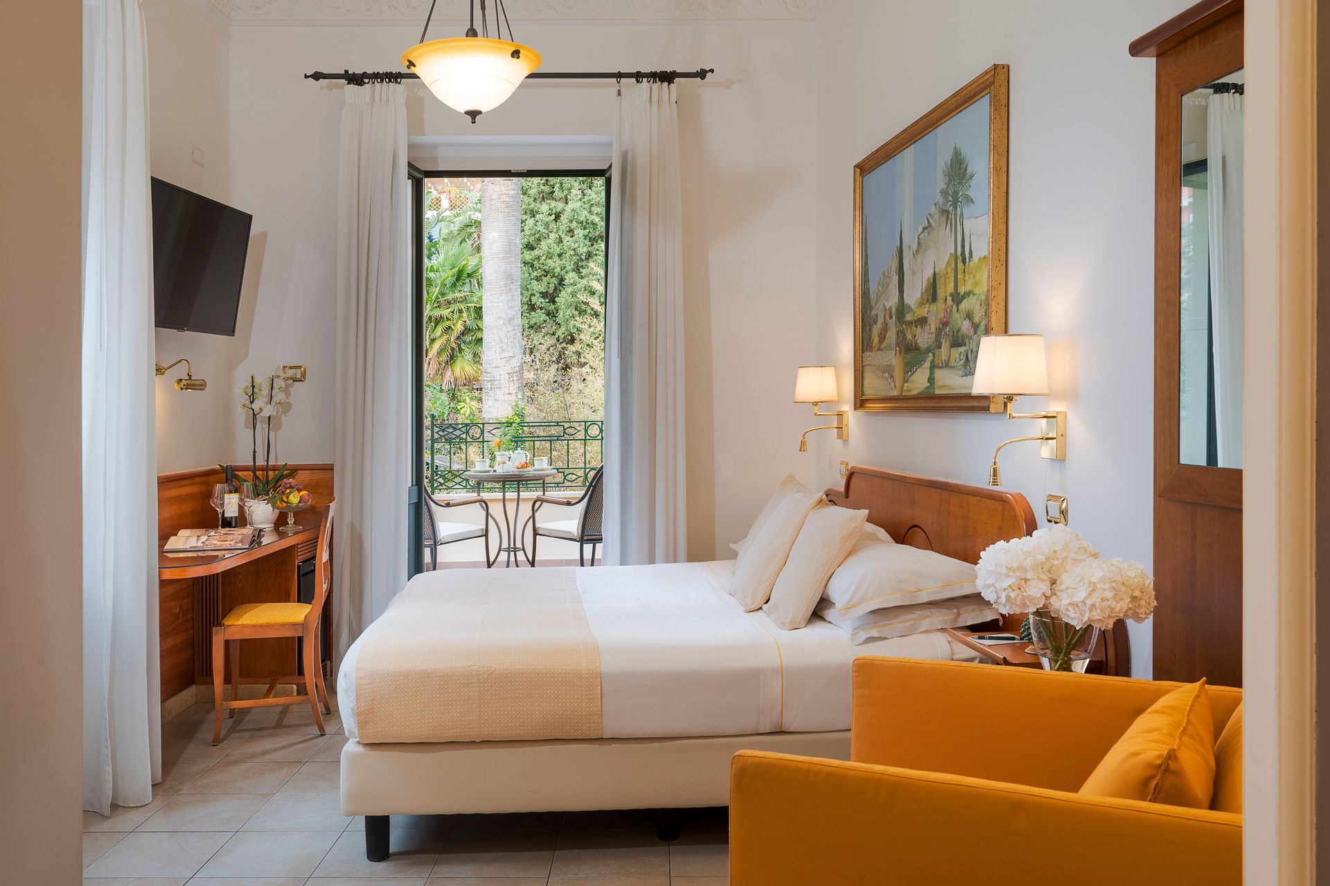 Chambre lumineuse avec un lit, une chaise moutarde, un bureau, des œuvres d'art et des portes-fenêtres