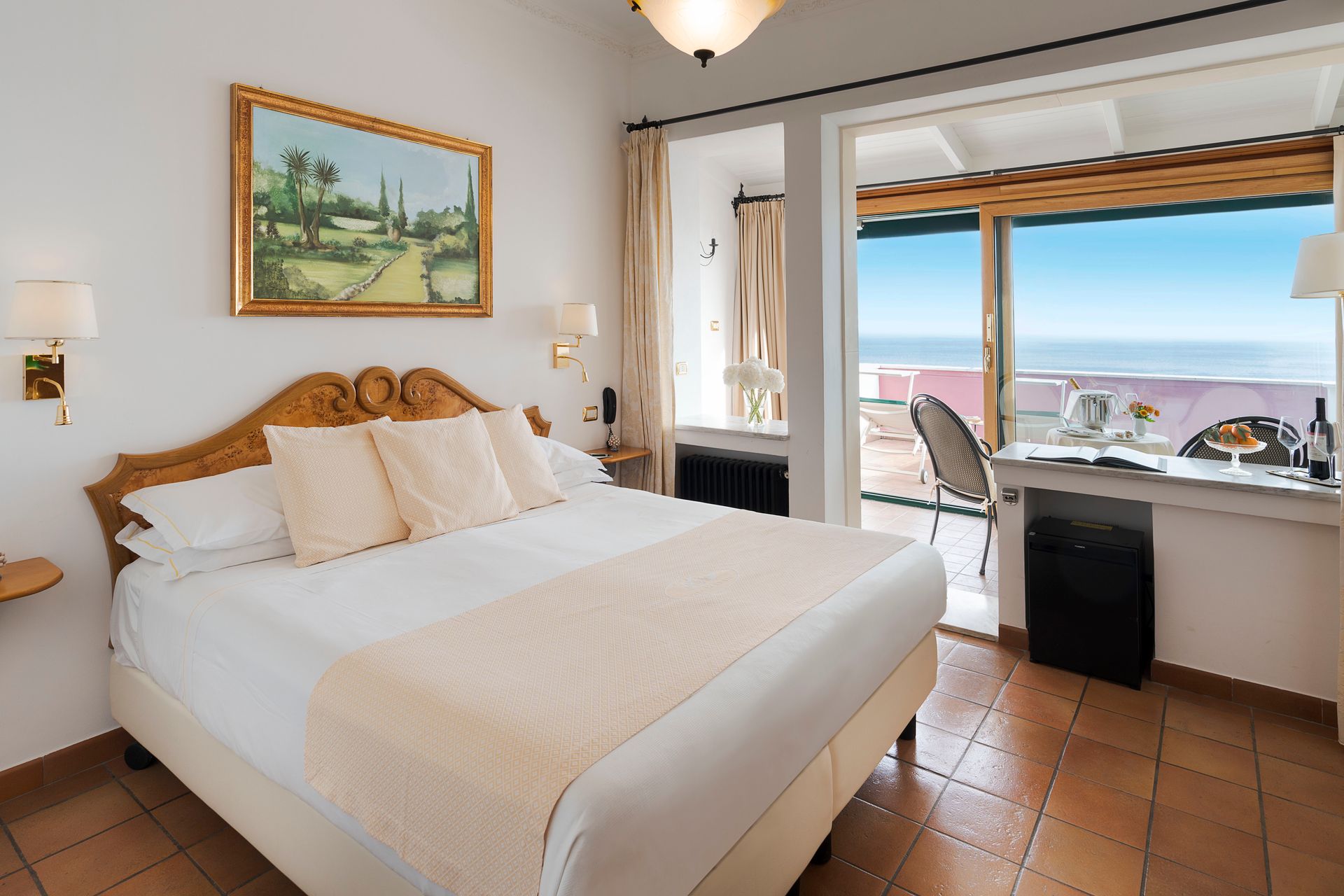 Bright bedroom with a bed, terracotta tile floor, and an open window overlooking the sea.