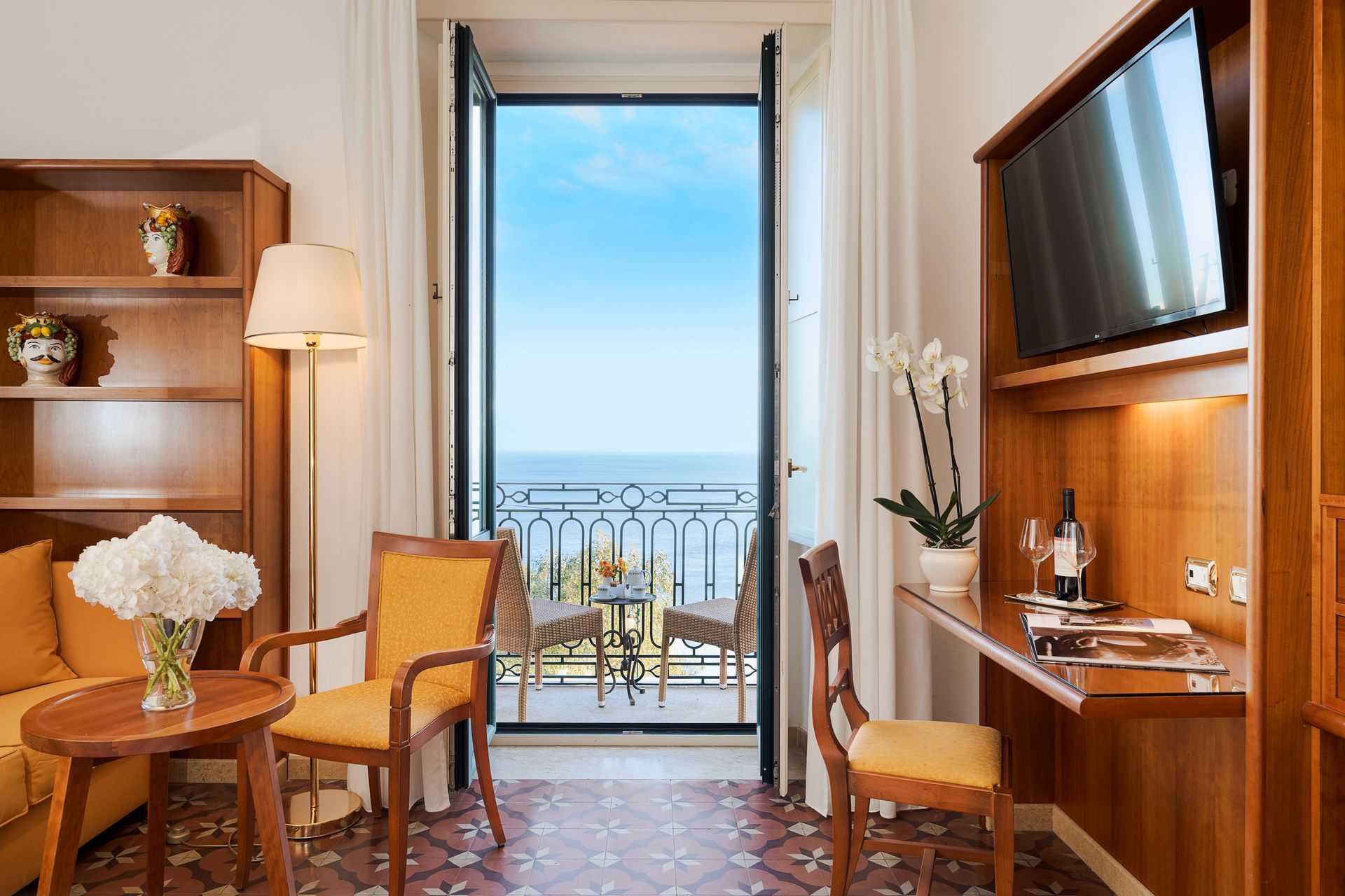 Elegant hotel room with balcony sea view, wooden furniture, and warm lighting