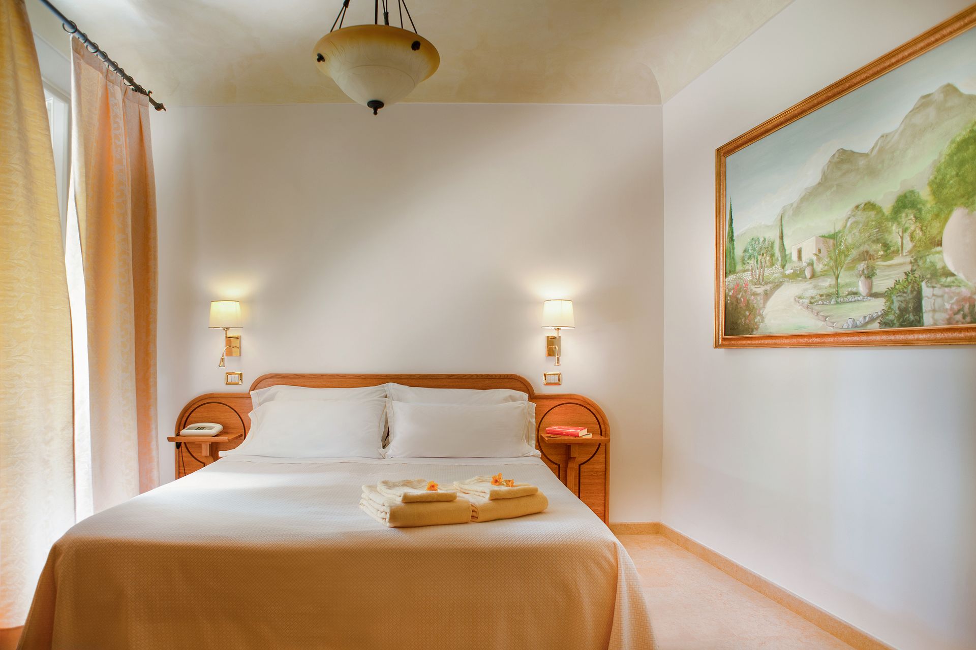 Bright bedroom with a double bed, bedside lamps, and a framed landscape painting on the wall.