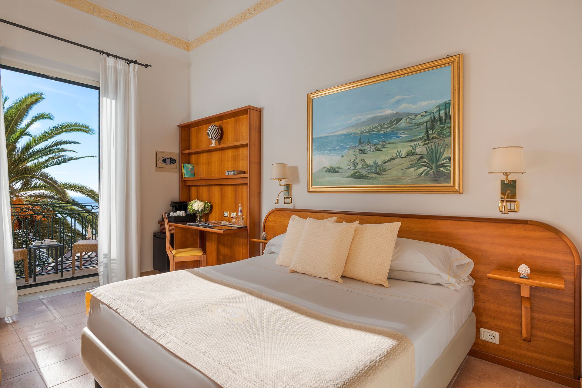 Chambre lumineuse avec lit, balcon avec vue sur l'océan et palmiers à l'extérieur de la fenêtre.