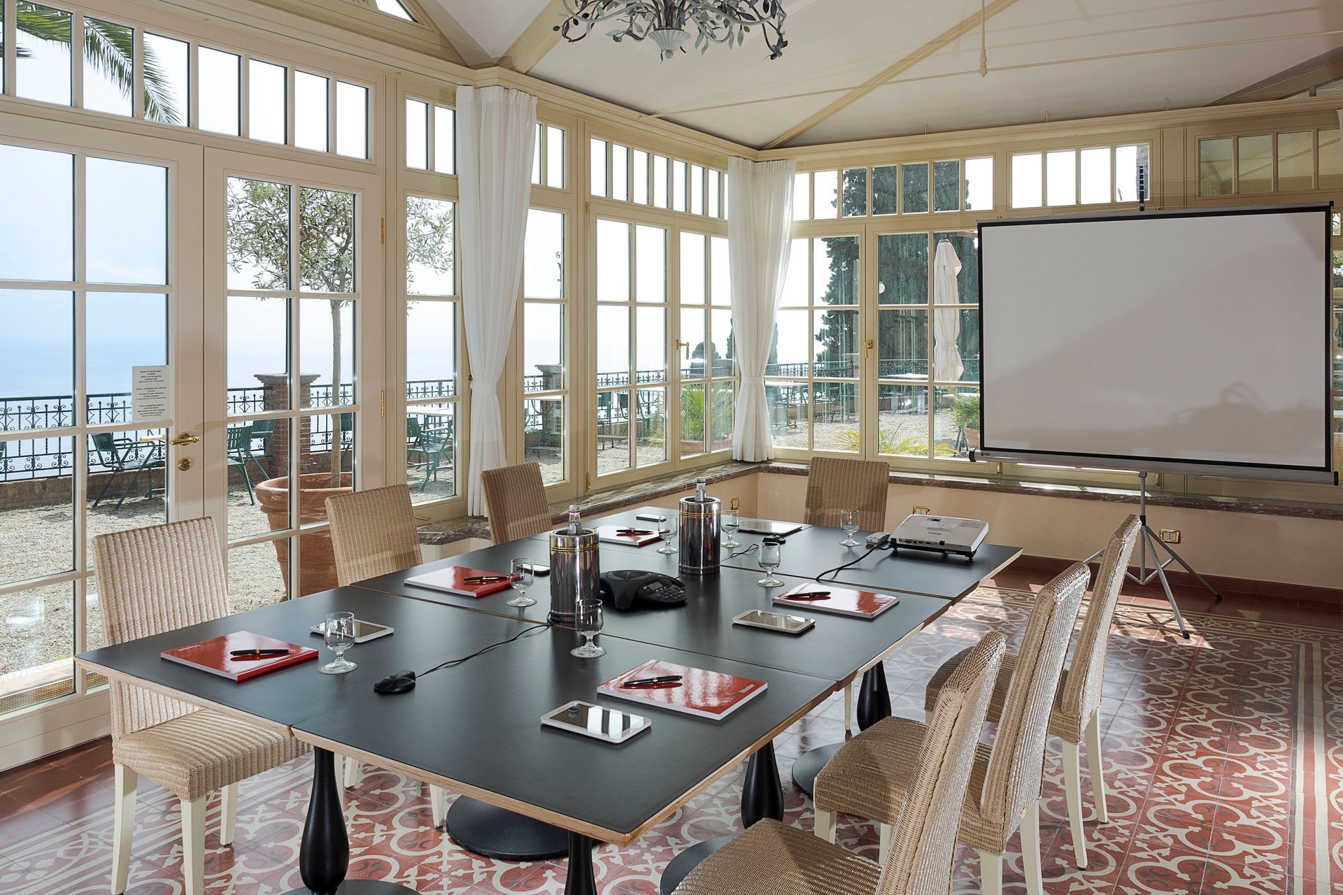 Bright conference room with glass walls, long table, chairs, and a projector screen overlooking water