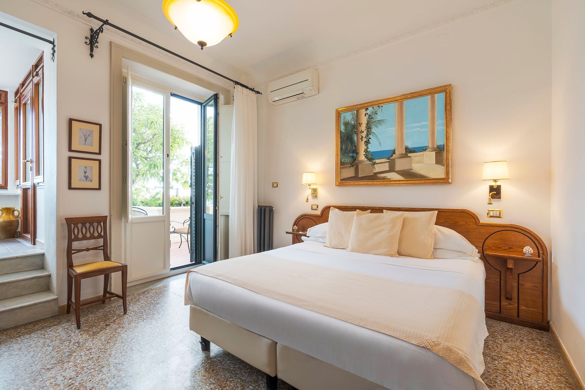 Bright bedroom with white bed, wicker nightstands, wall art, and open balcony doors.