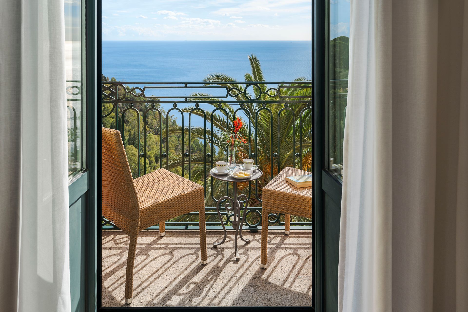 Balcony with wicker chairs and table overlooking the ocean through open curtains