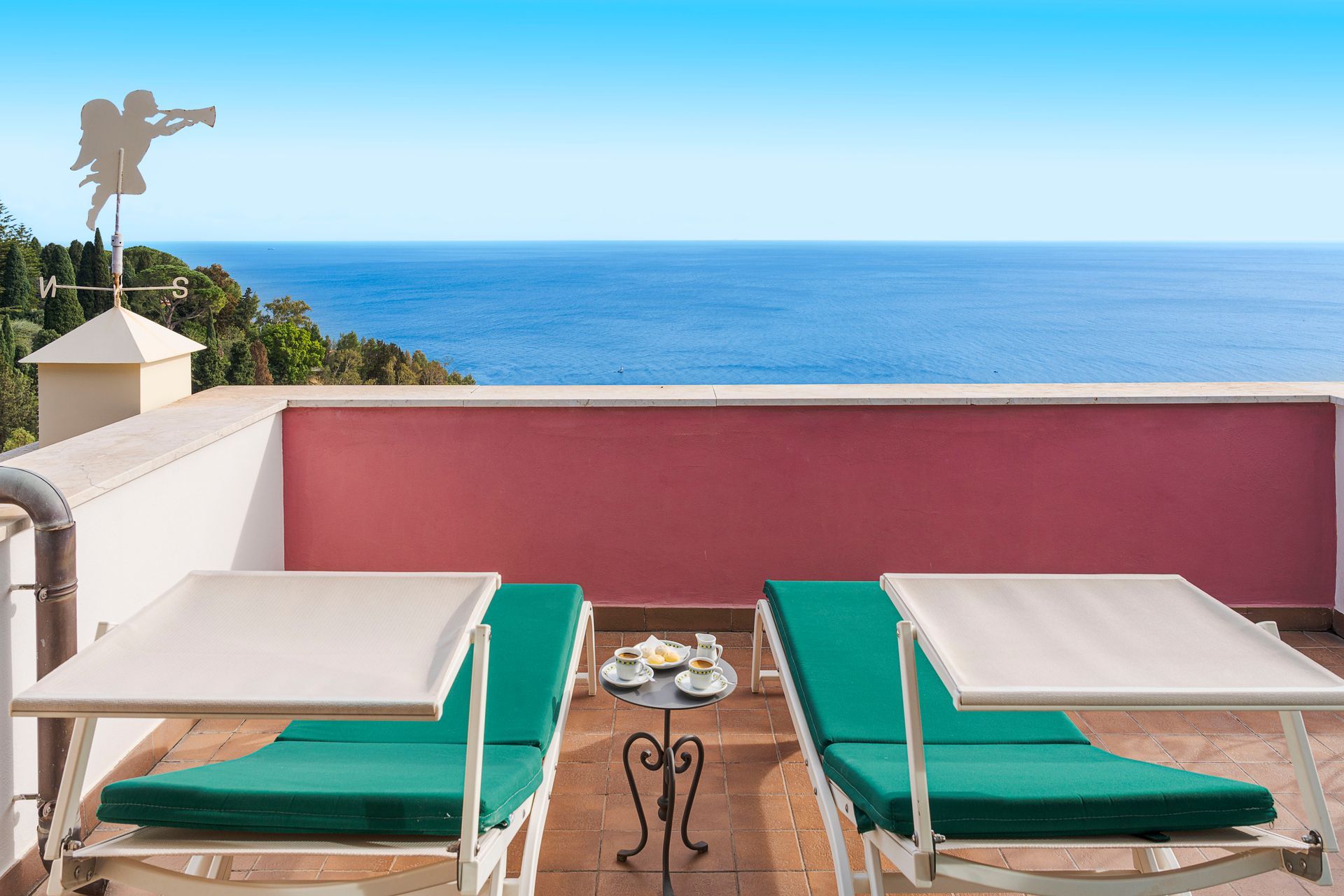 Two green lounge chairs on a terrace overlooking the blue ocean under a clear sky