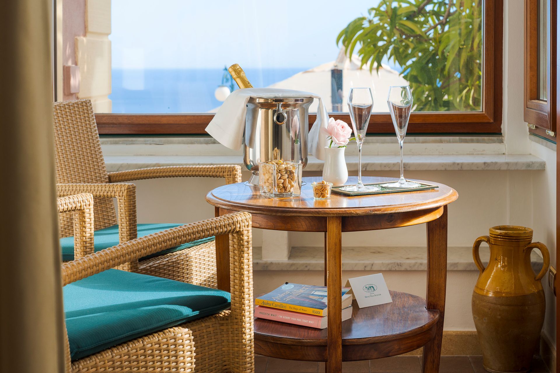 Wicker chair and round table by a bright window, with tea service, glassware, and a potted plant