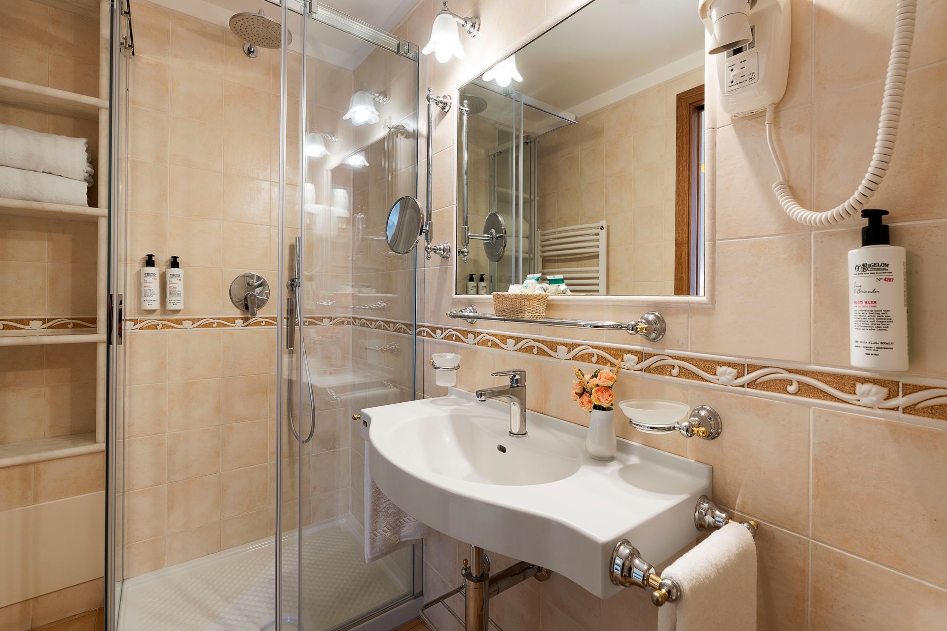 Compact beige-tiled bathroom with glass shower, wall mirror, and white sink vanity.