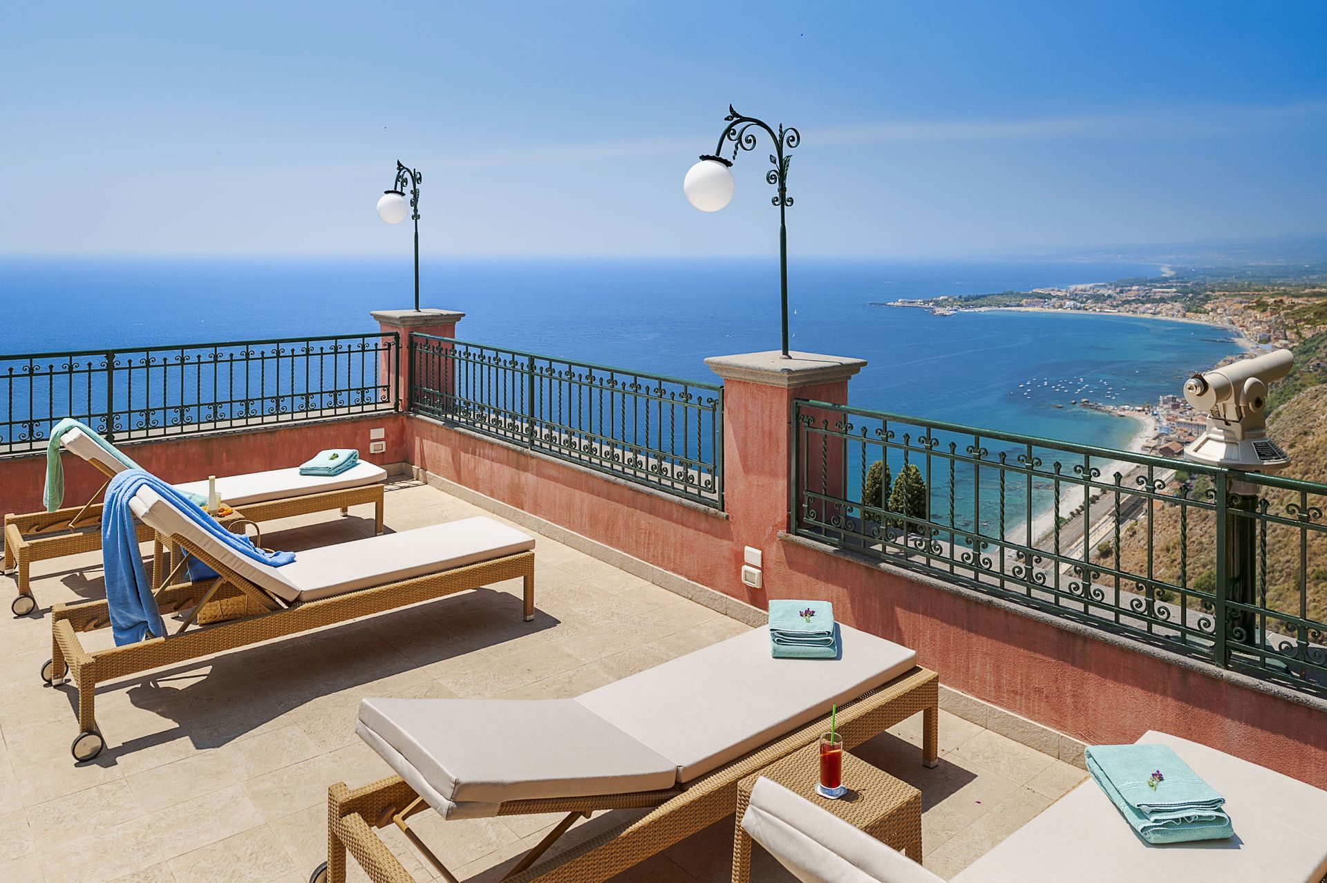 Terrace with lounge chairs overlooking a blue ocean and coastline under a clear sky