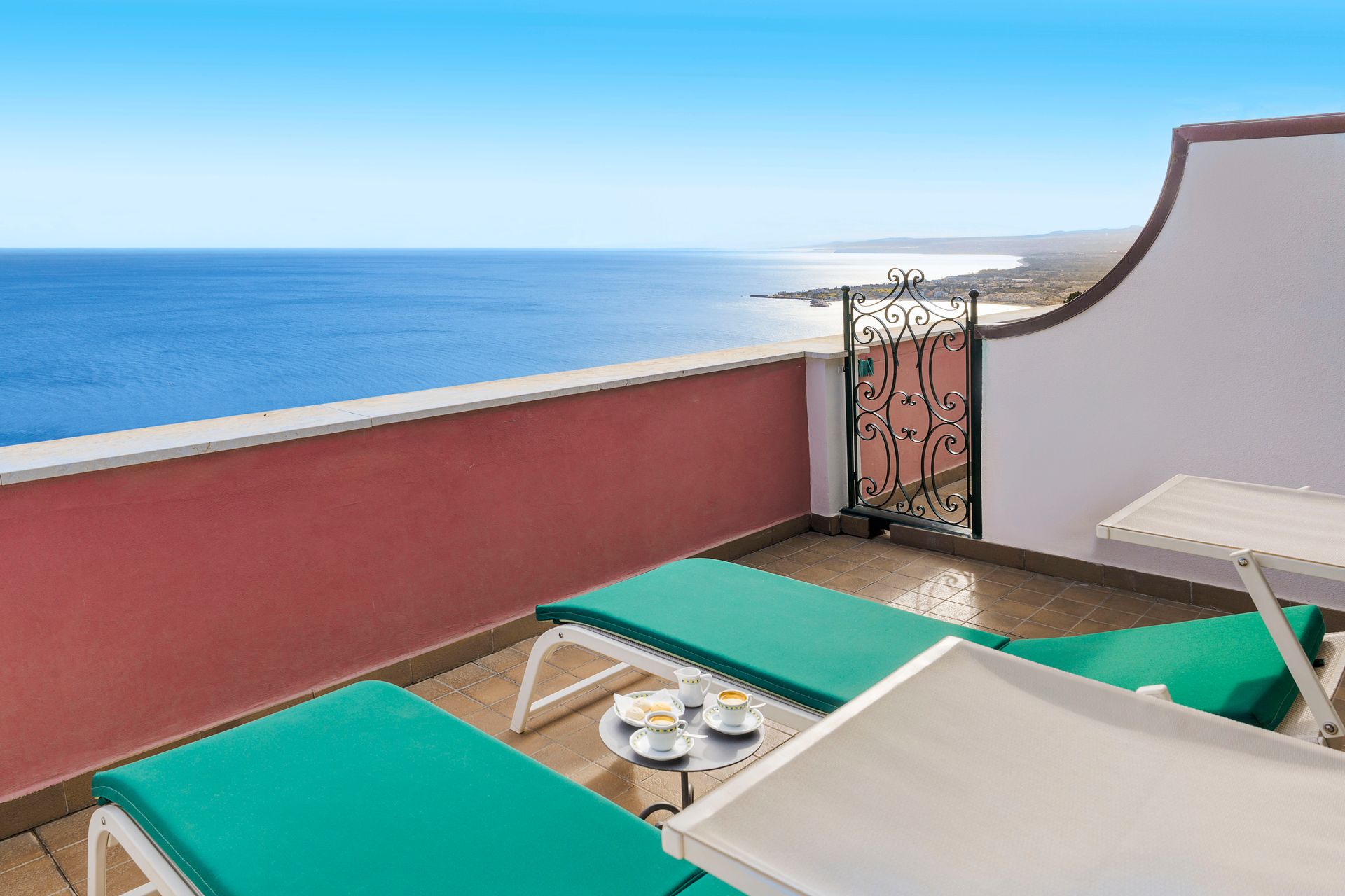 Balcony lounge chairs facing the ocean, with a table and a bright blue sky.