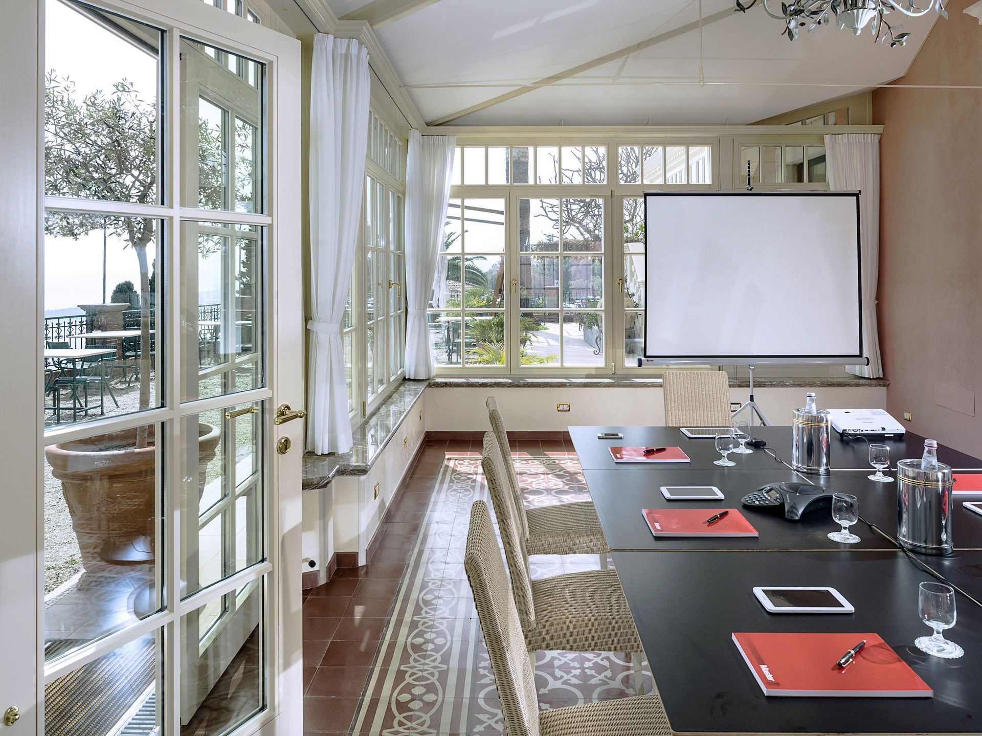 Bright meeting room with long conference table, projector screen, and large windows overlooking outdoors
