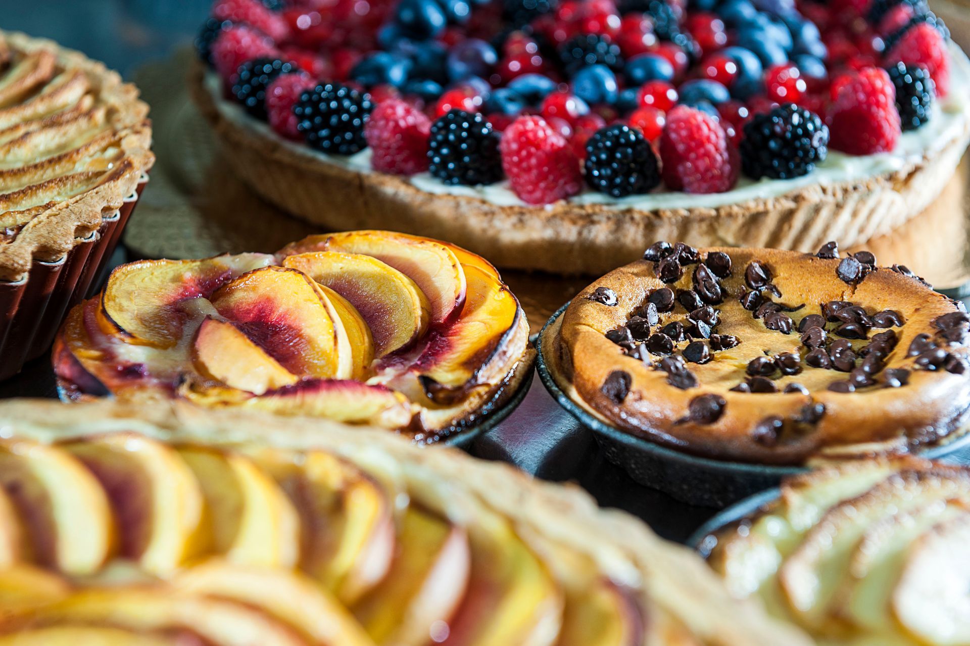 Assorted fruit tarts and pies with berries, peaches, and chocolate chips on display