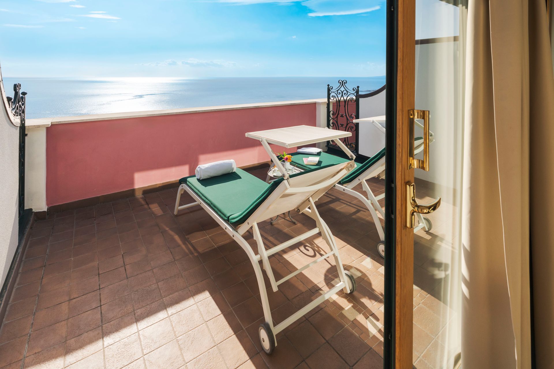 Sunlit balcony with two lounge chairs, ocean view, and open door