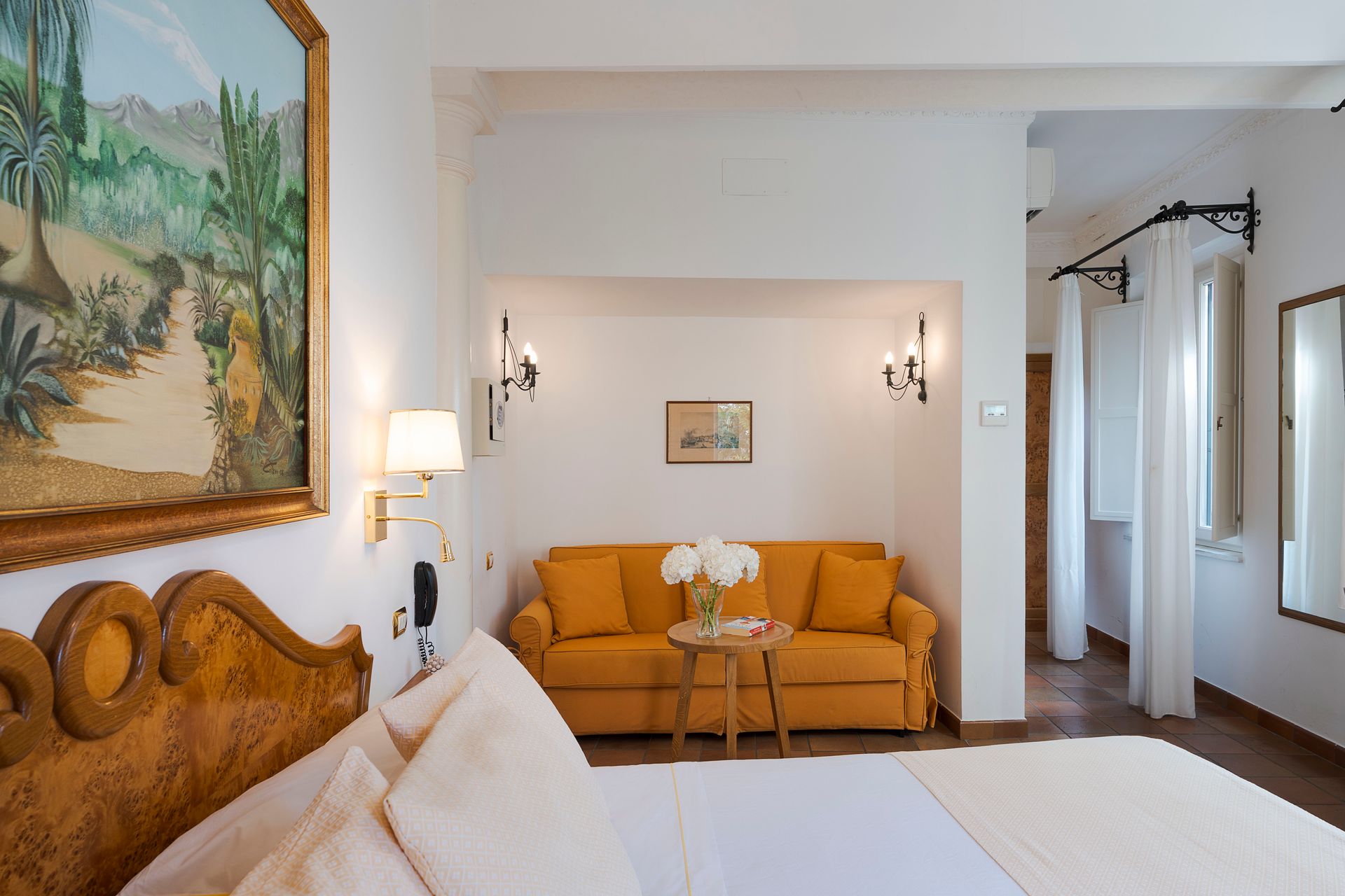 Hotel room with carved wooden bed, orange sofa, and soft white decor