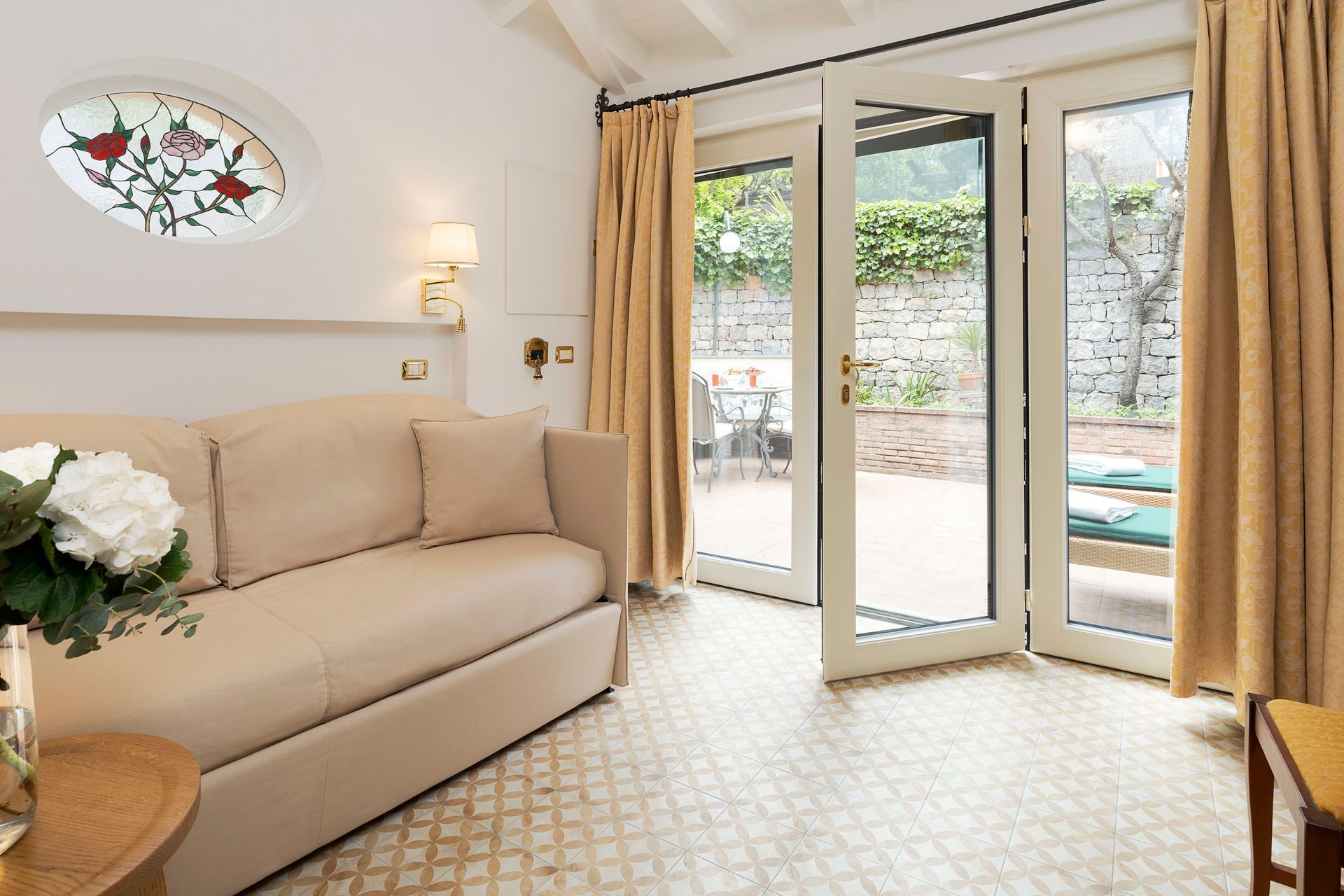 Bright living room with beige sofa, patterned floor, and open glass doors to a garden patio