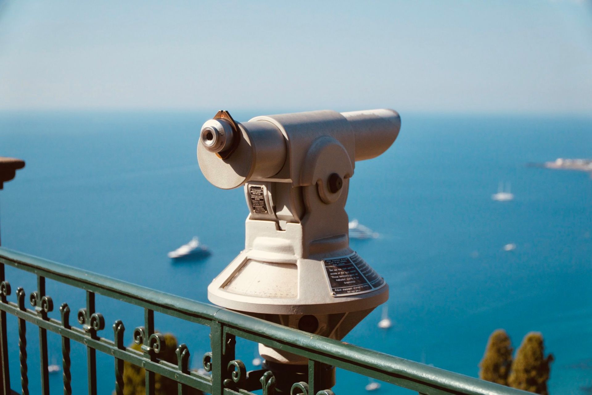 Coin-operated telescope overlooking a blue sea from a seaside railing