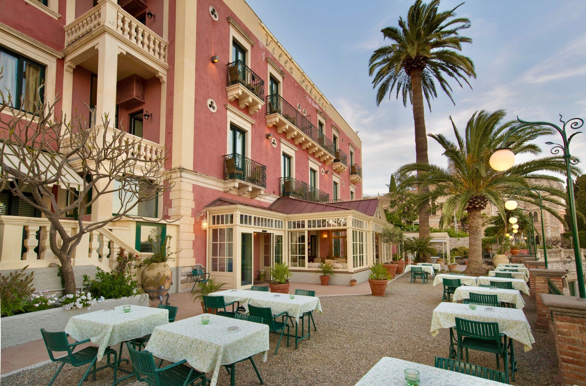 Courtyard café with pink building, palm trees, and white tablecloth tables outdoors