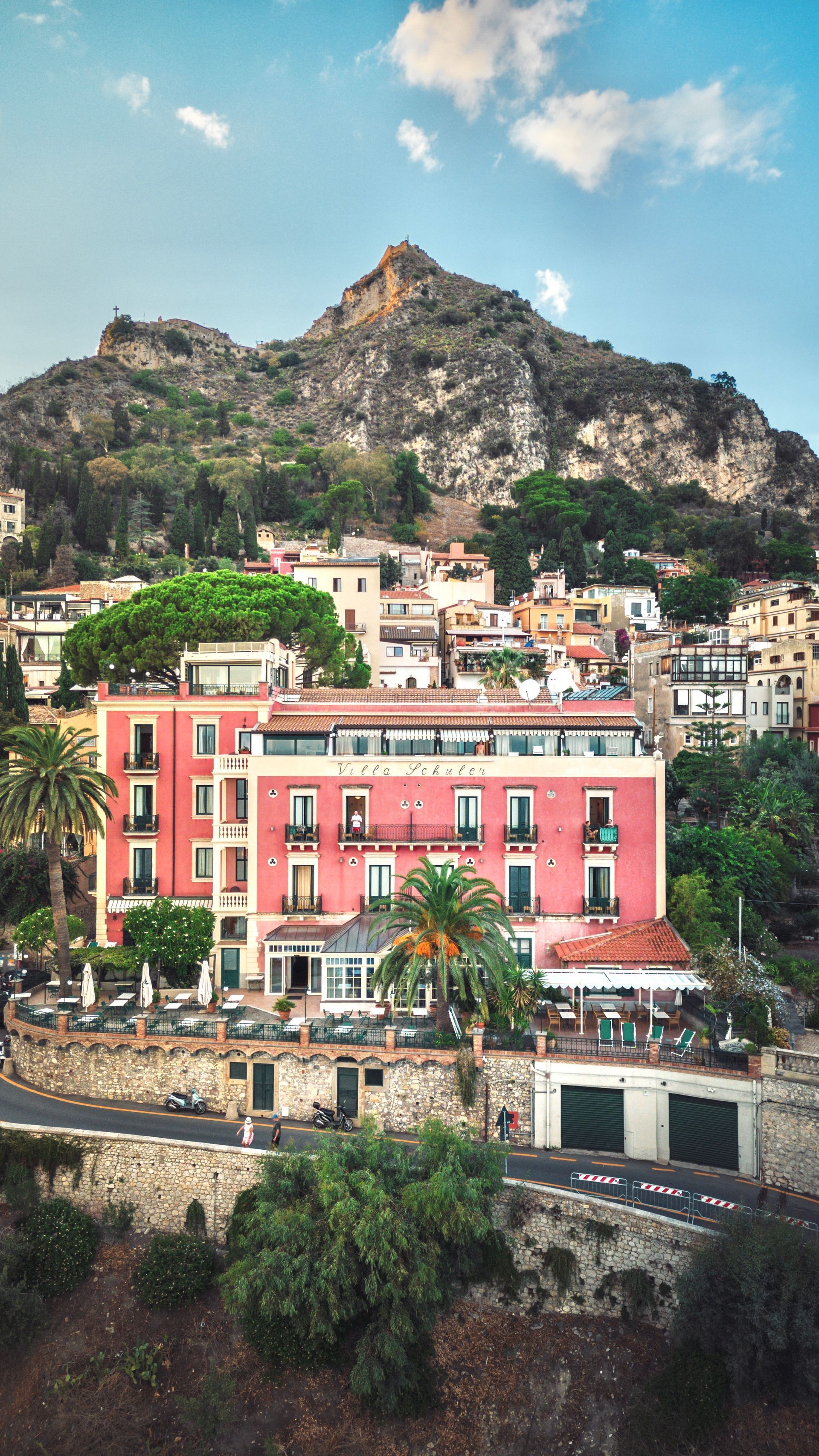 Colorful hillside town with pink buildings below a rocky mountain under a blue sky
