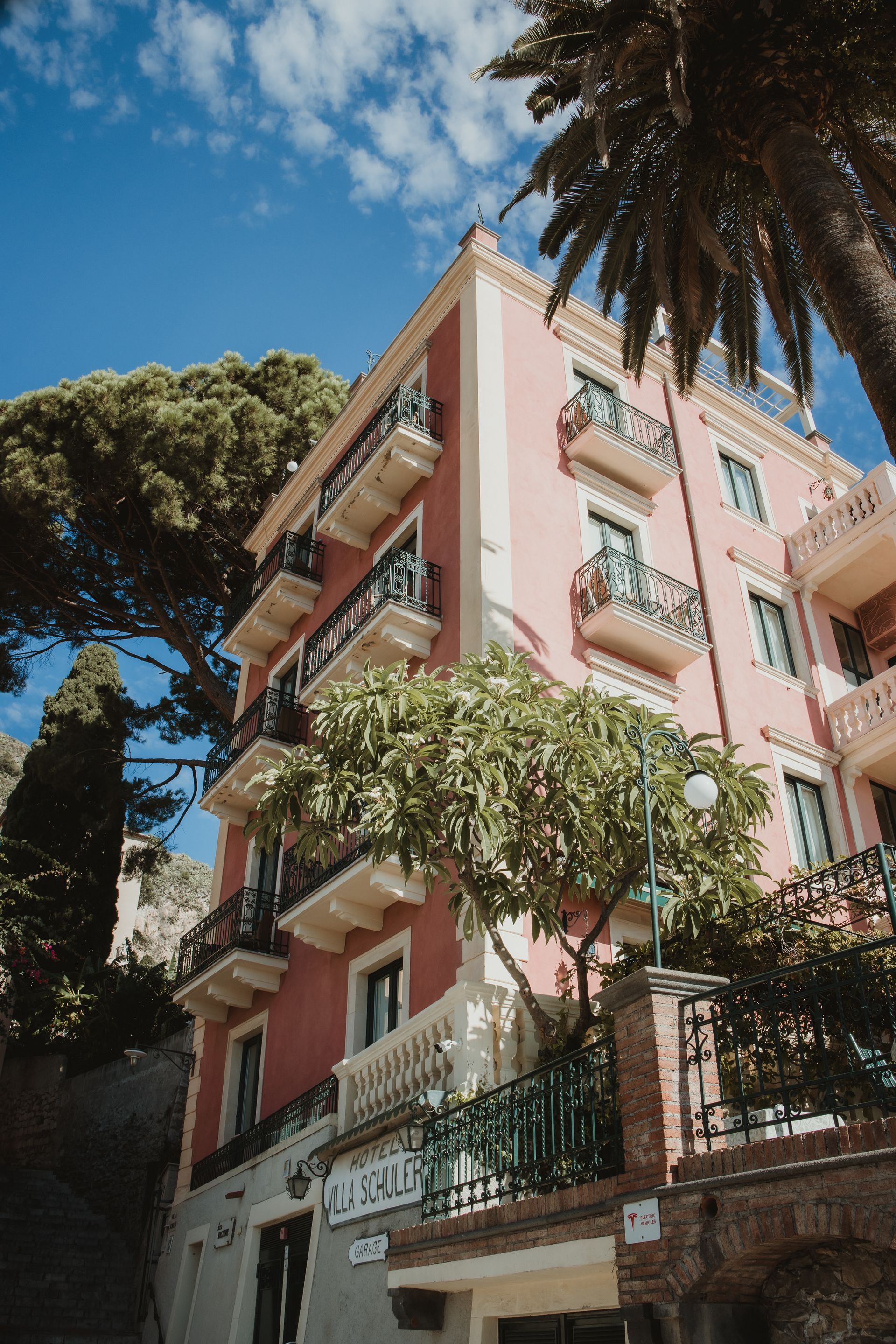 Pink apartment building with balconies and trees against a blue sky